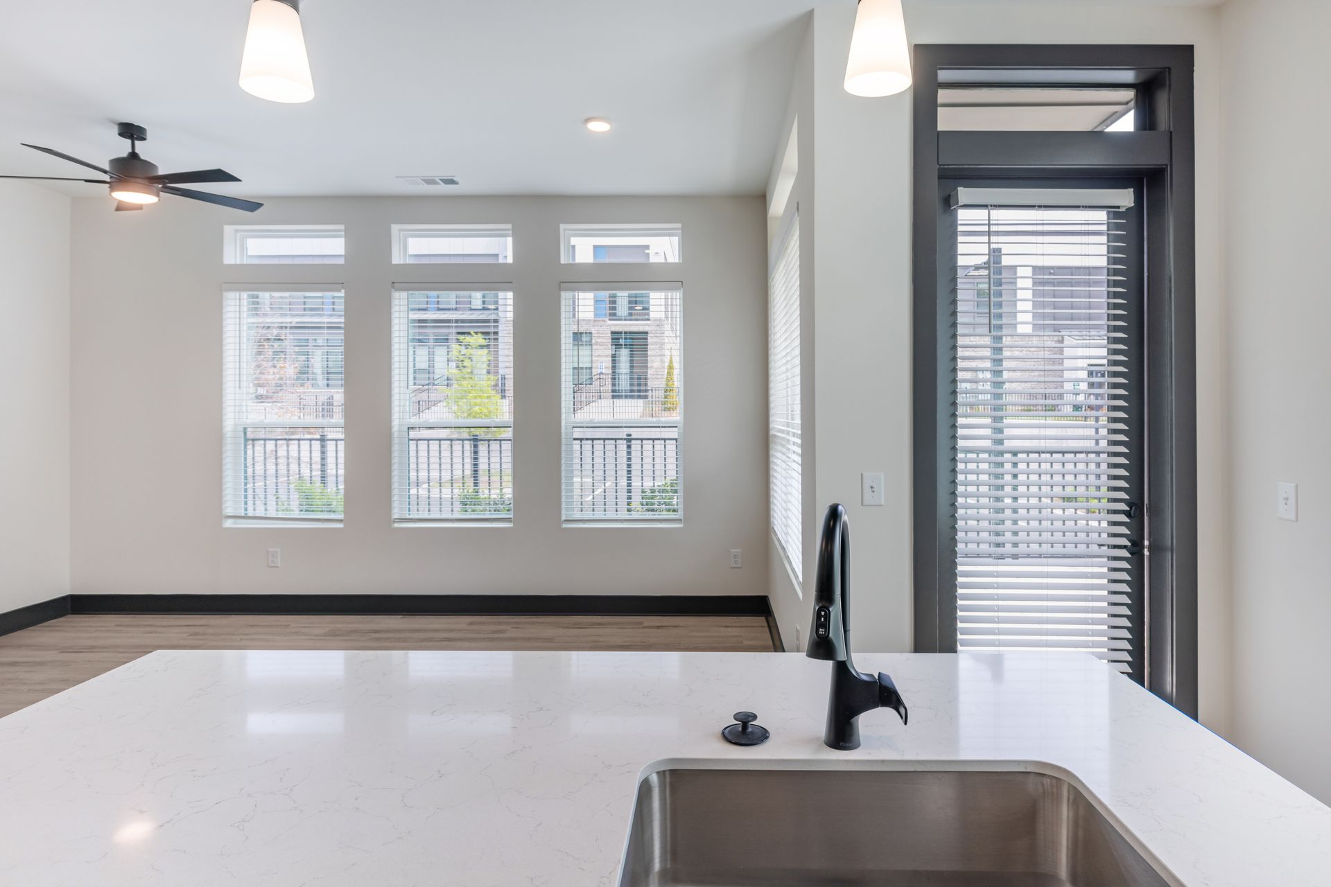 Bright modern kitchen with white counters, sink, and large windows overlooking a balcony at Vela Park apartments in East Lake, Atlanta, GA.