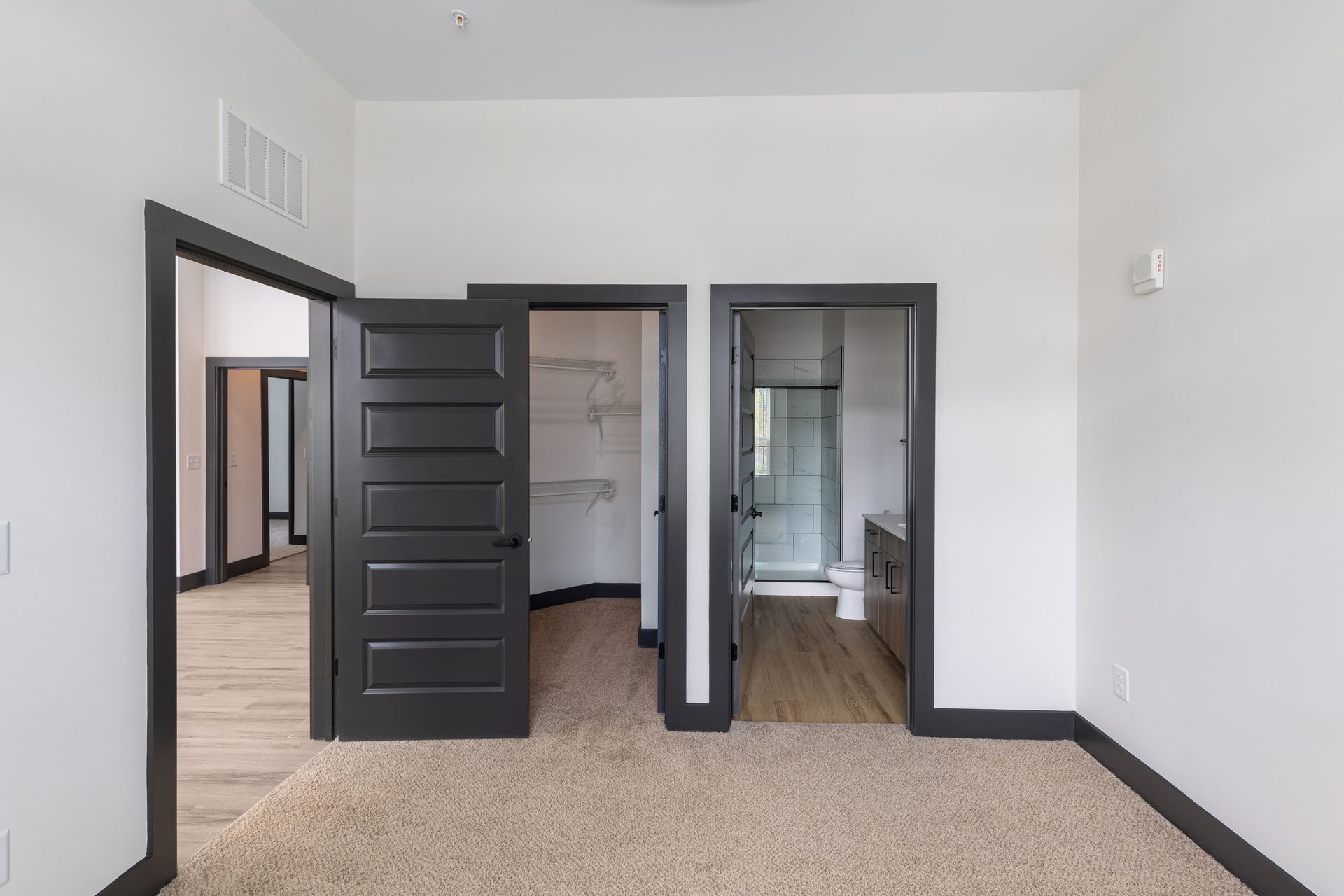 Empty bedroom with black door, carpet, and two closet openings, one showing a bathroom at Vela Park apartments in East Lake, Atlanta, GA.