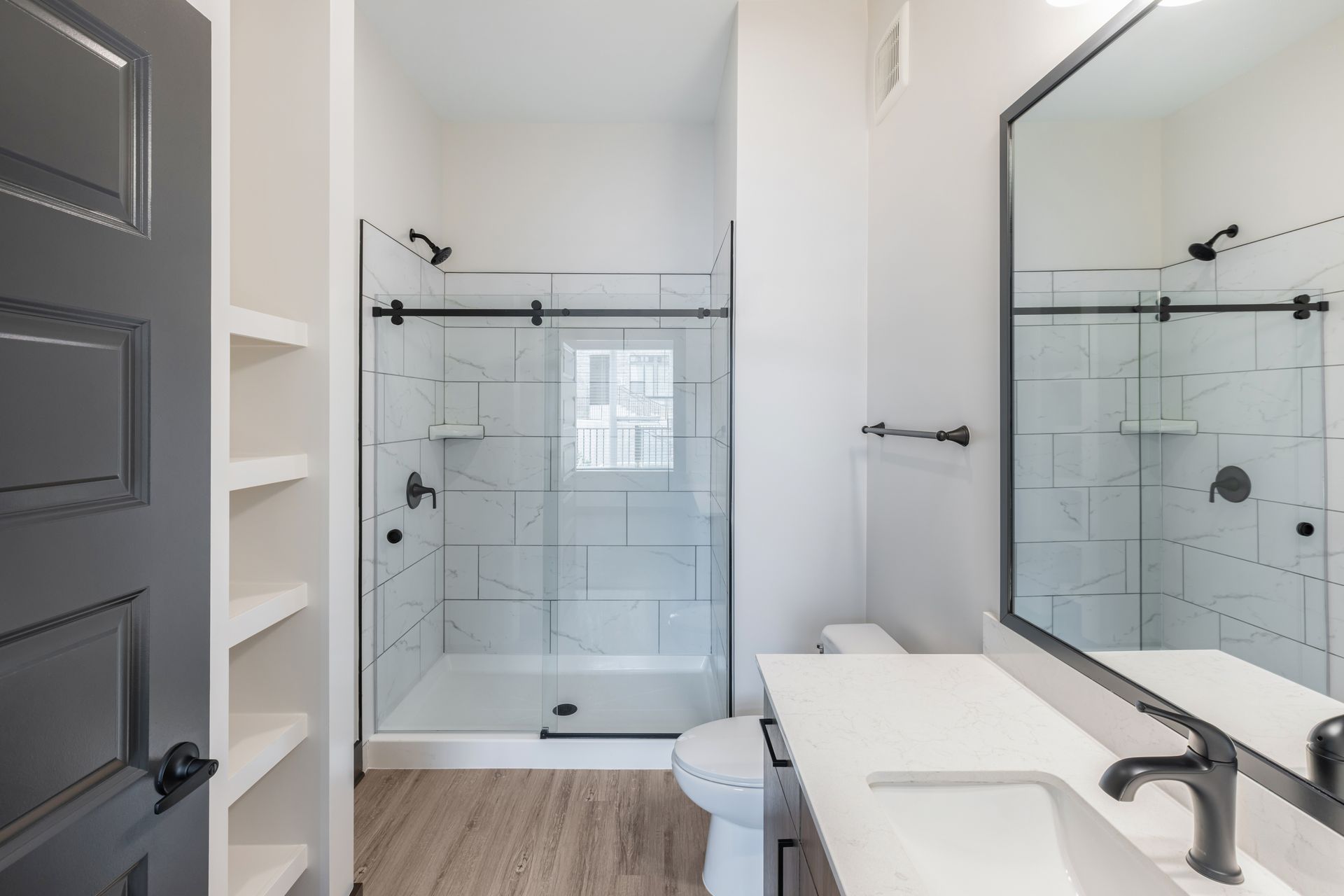 Bright modern bathroom with glass shower, double vanity, mirror, and white walls at Vela Park apartments in East Lake, Atlanta, GA.