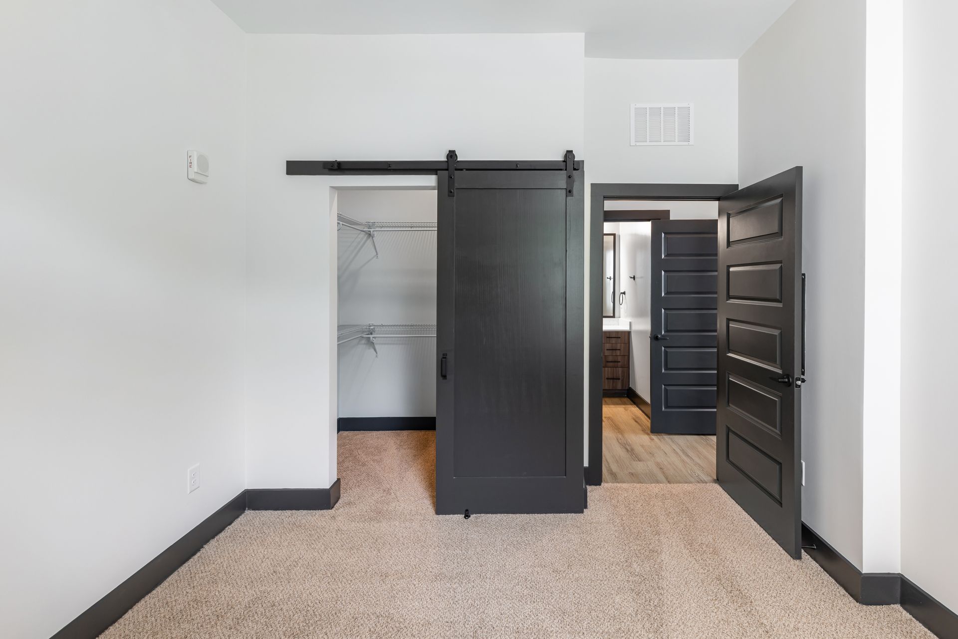 Empty room with an open closet, dark sliding door, and an open black entry door at Vela Park apartments in East Lake, Atlanta, GA.
