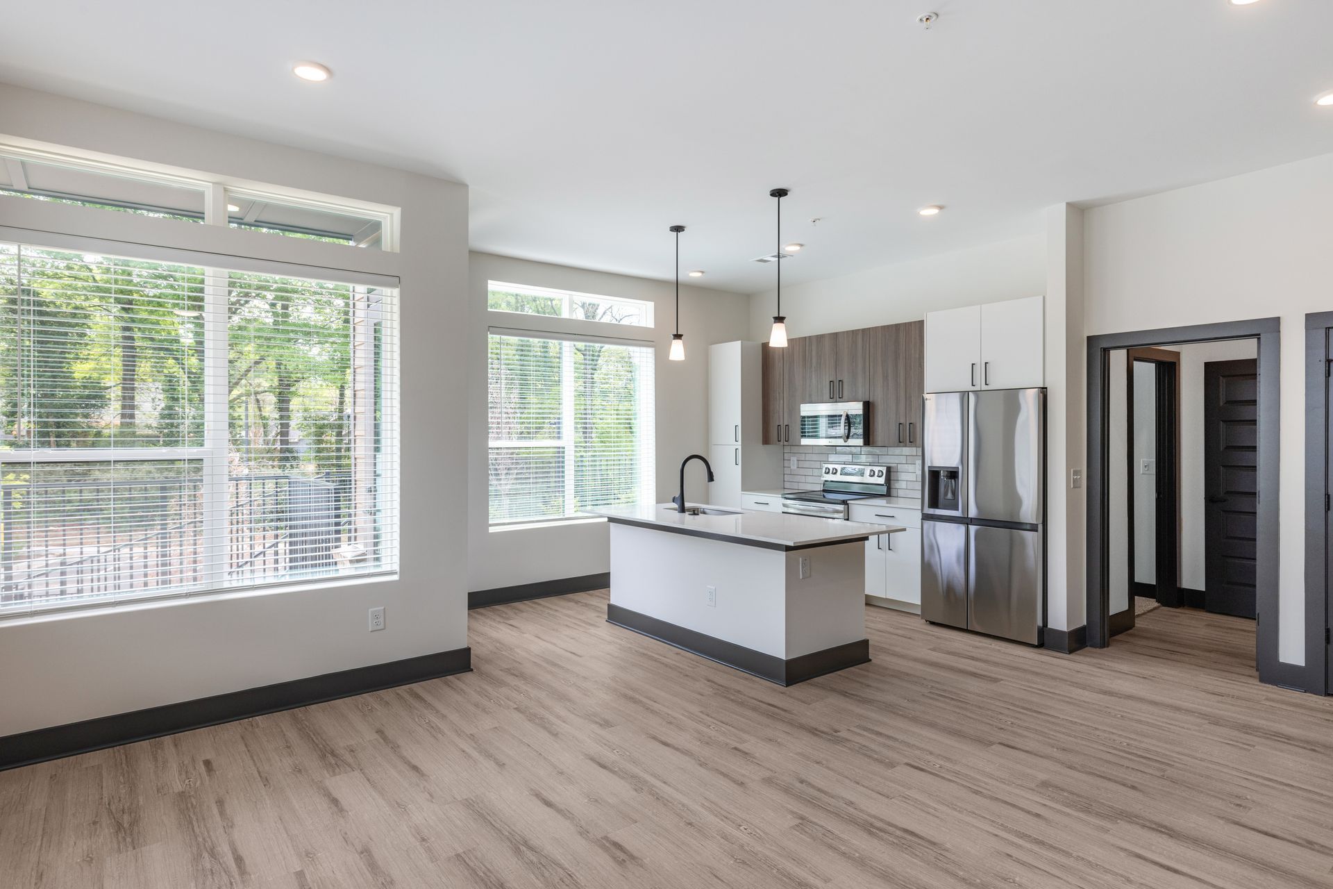Bright open kitchen with island, stainless steel appliances, wood floors, and large windows at Vela Park apartments in East Lake, Atlanta, GA.