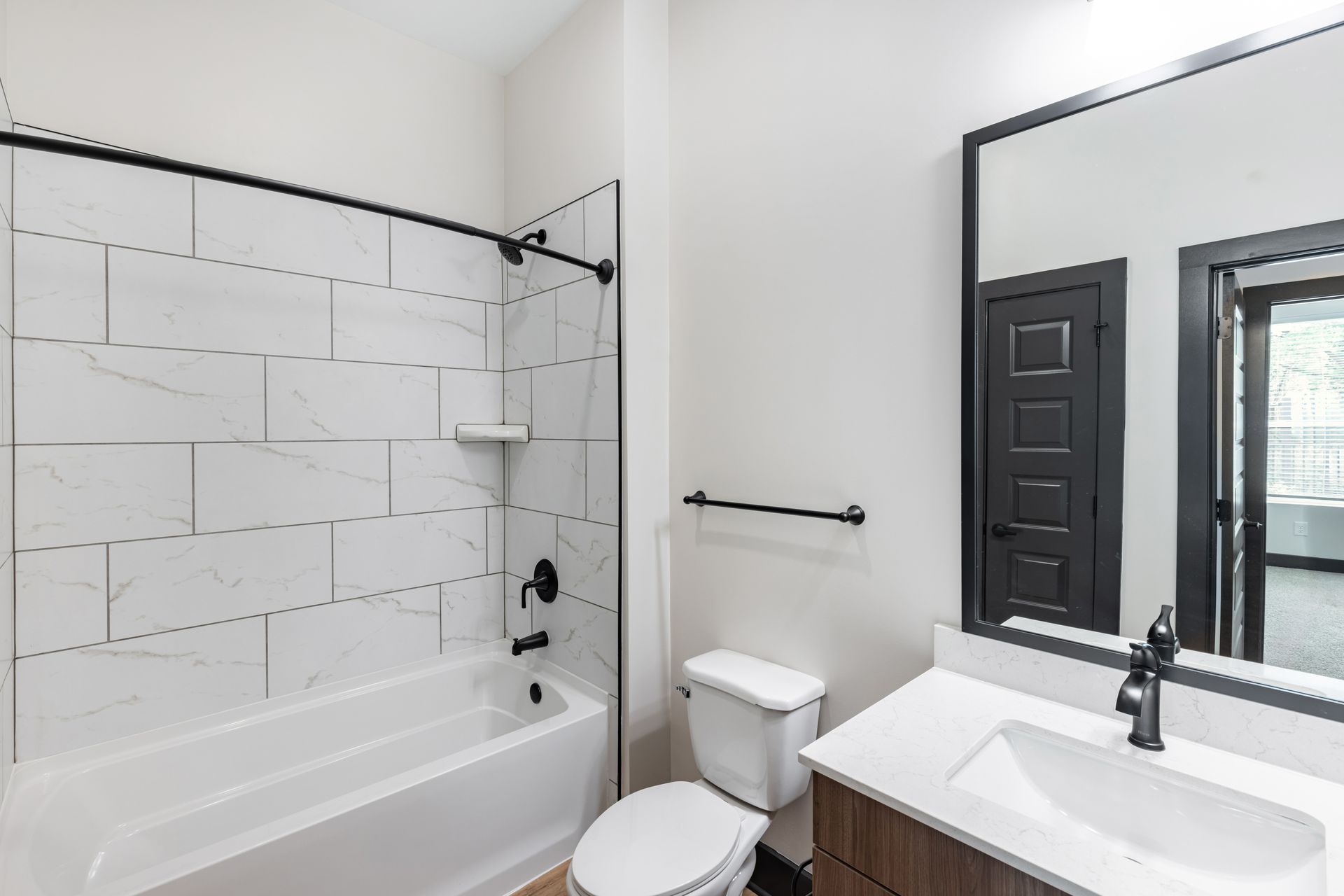 Modern white bathroom with tub-shower, toilet, sink, and large mirror at Vela Park apartments in East Lake, Atlanta, GA.