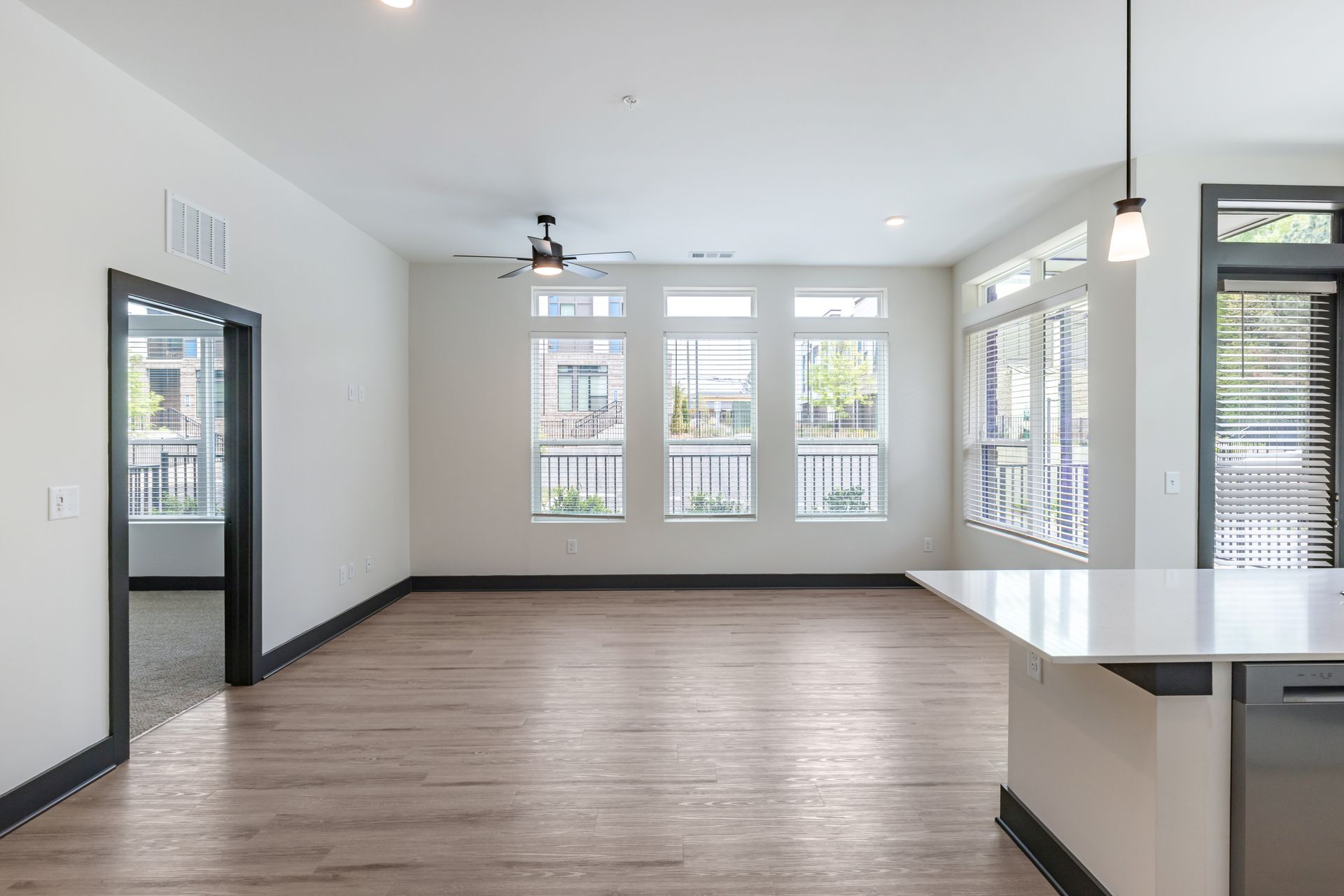 Empty modern living room with wood floors, white walls, large windows, and a kitchen island edge in the foreground at Vela Park apartments in East Lake, Atlanta, GA.