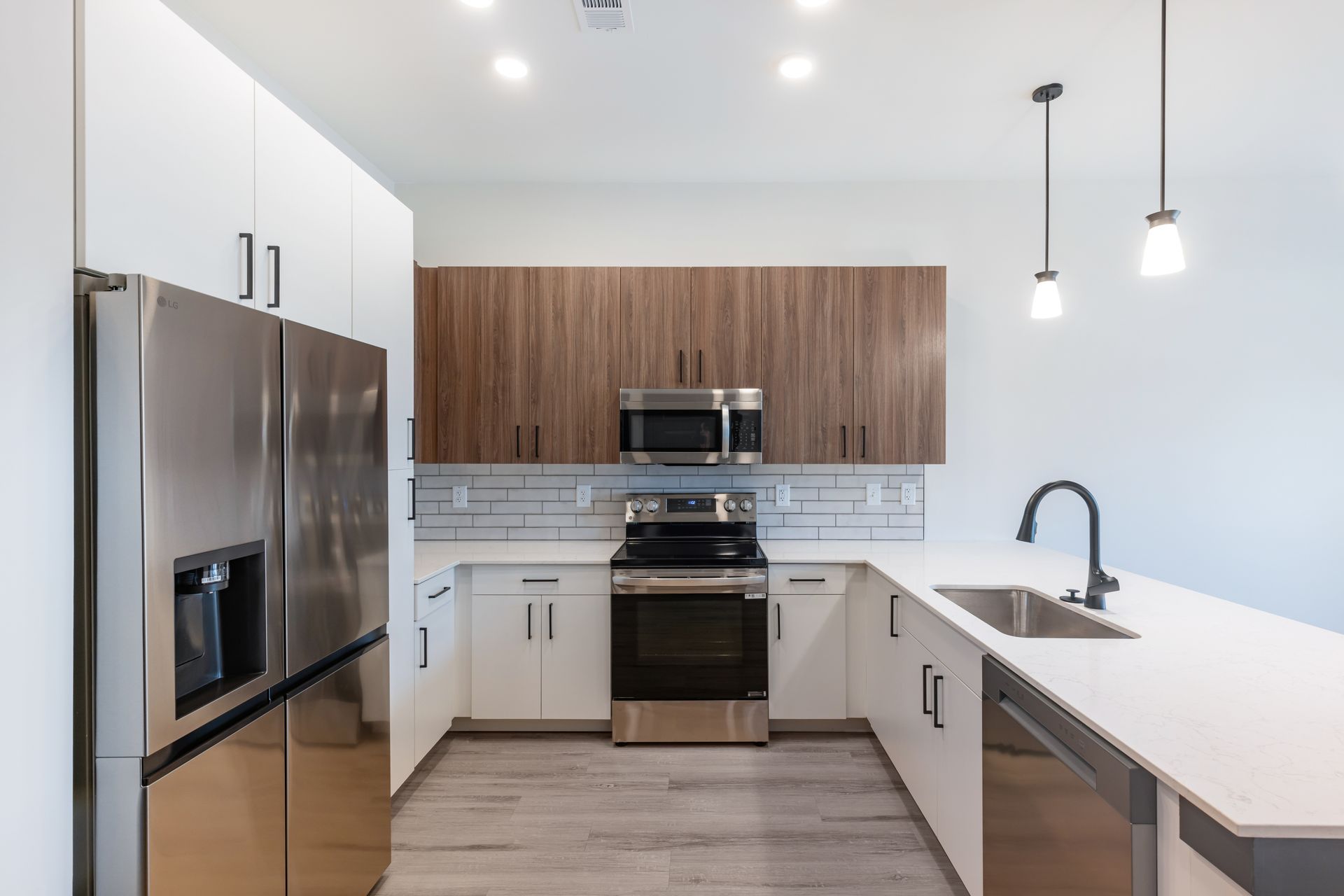 Modern kitchen with stainless steel appliances, white cabinets, wood backsplash, and white countertops at Vela Park apartments in East Lake, Atlanta, GA.