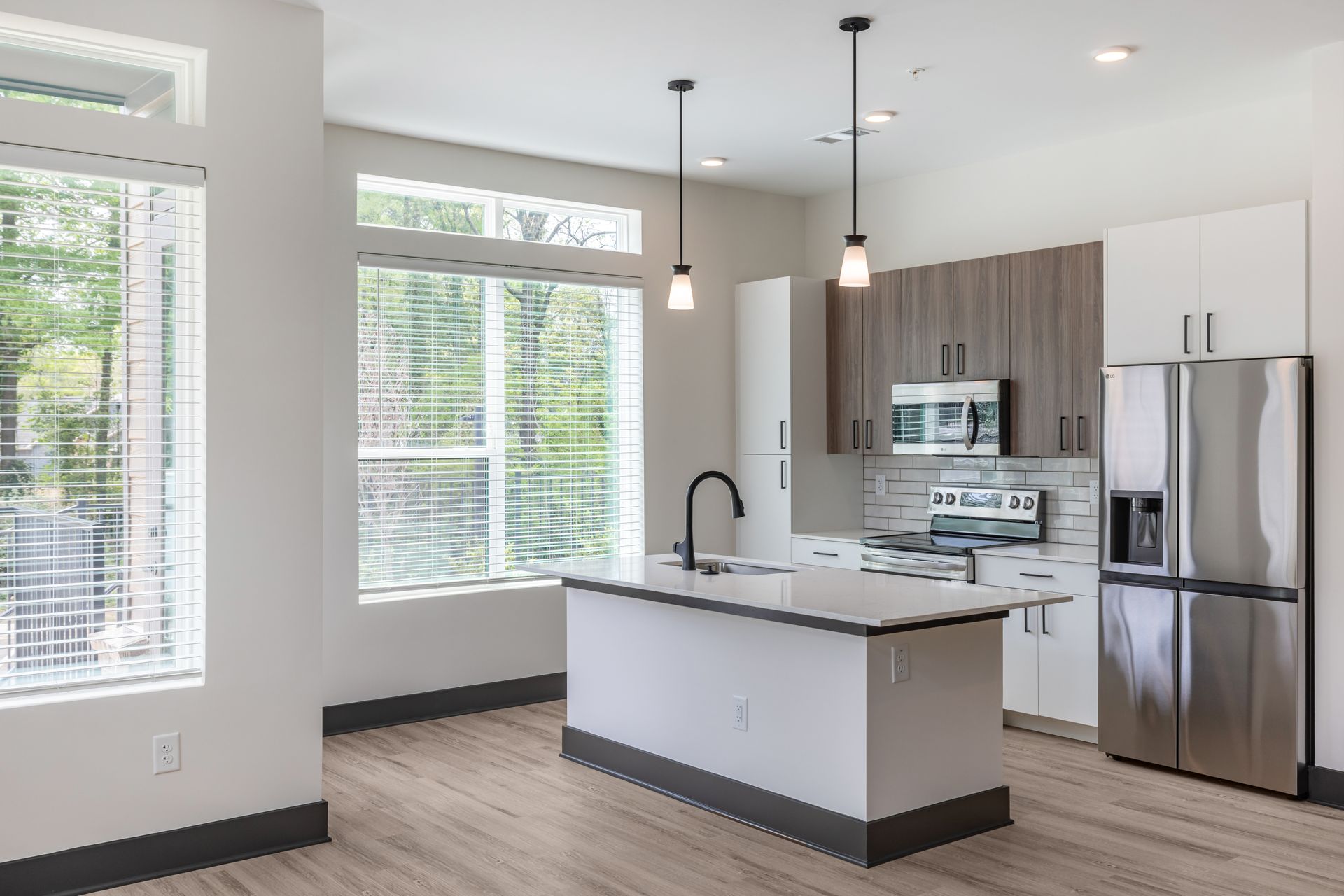Modern open-plan kitchen with white island, stainless steel appliances, and large windows at Vela Park apartments in East Lake, Atlanta, GA.