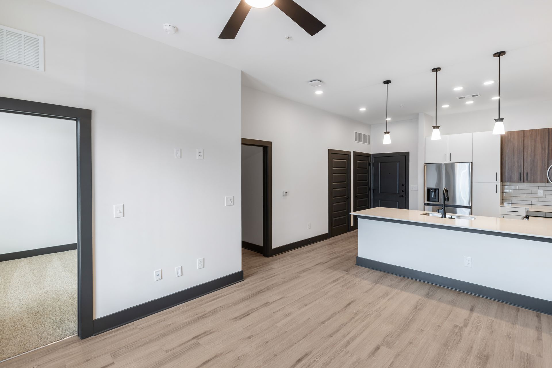 Bright modern kitchen and living area with white walls, wood floors, black trim, and island cabinets at Vela Park apartments in East Lake, Atlanta, GA.
