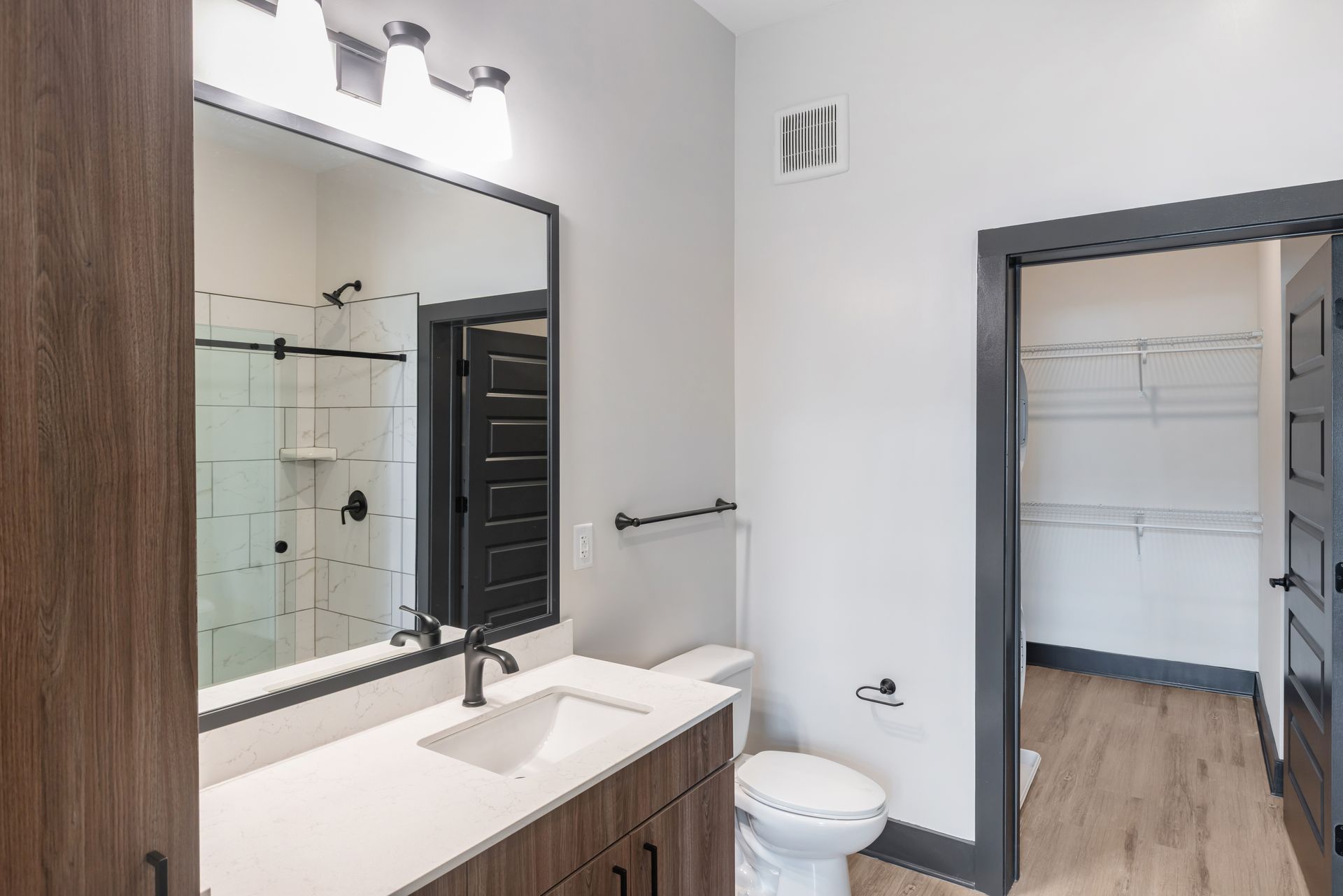 Modern bathroom with vanity mirror, white sink, toilet, and walk-in closet visible through doorway at Vela Park apartments in East Lake, Atlanta, GA.