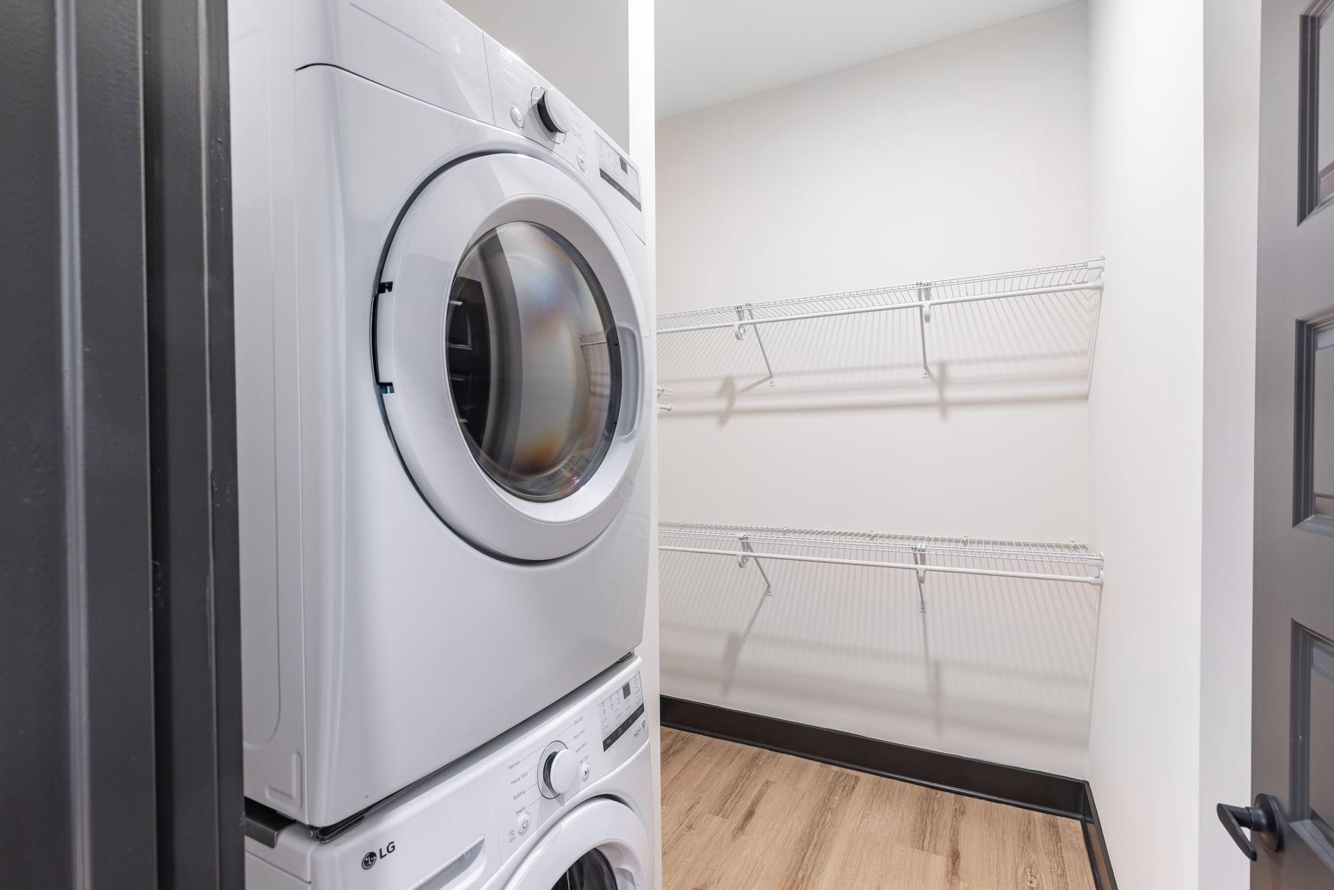 Laundry room with stacked washer and dryer beside wire shelving and wood floor at Vela Park apartments in East Lake, Atlanta, GA.