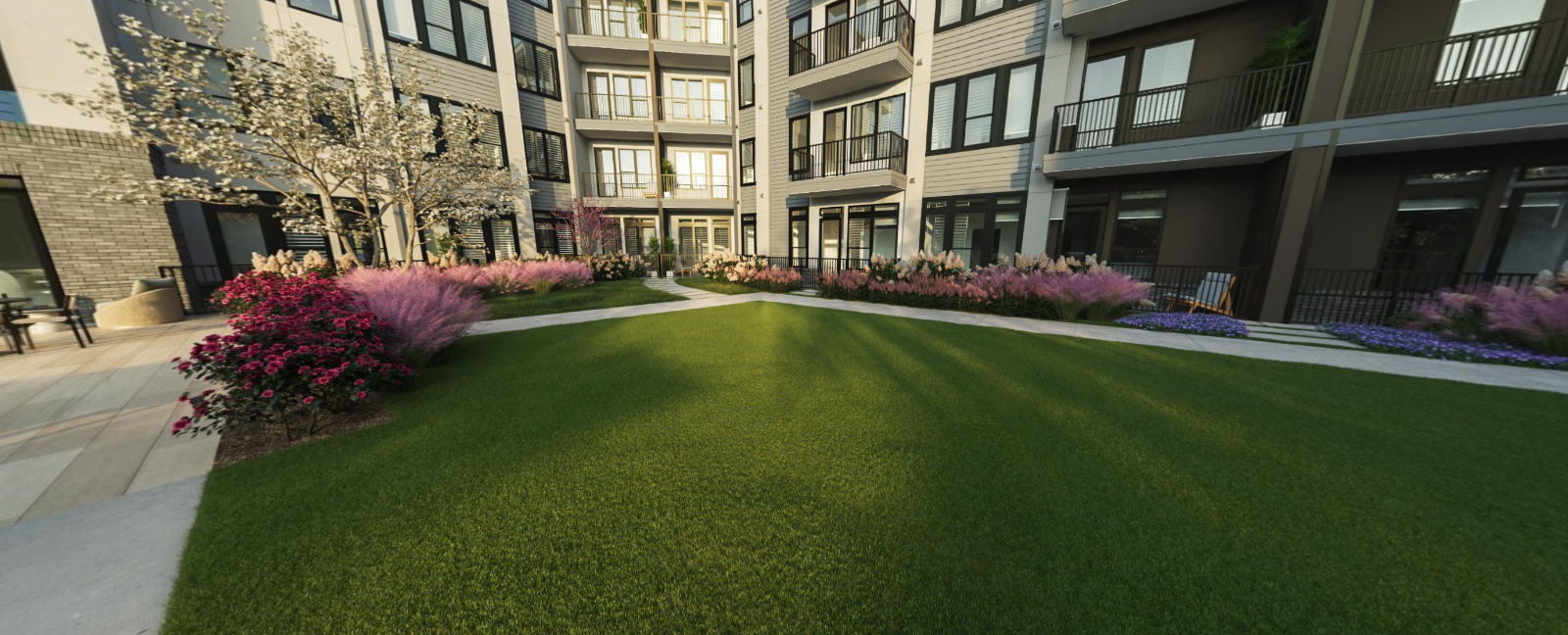 Apartment courtyard with bright green lawn, pink shrubs, and surrounding buildings at Vela Park apartments in East Lake, Atlanta, GA.