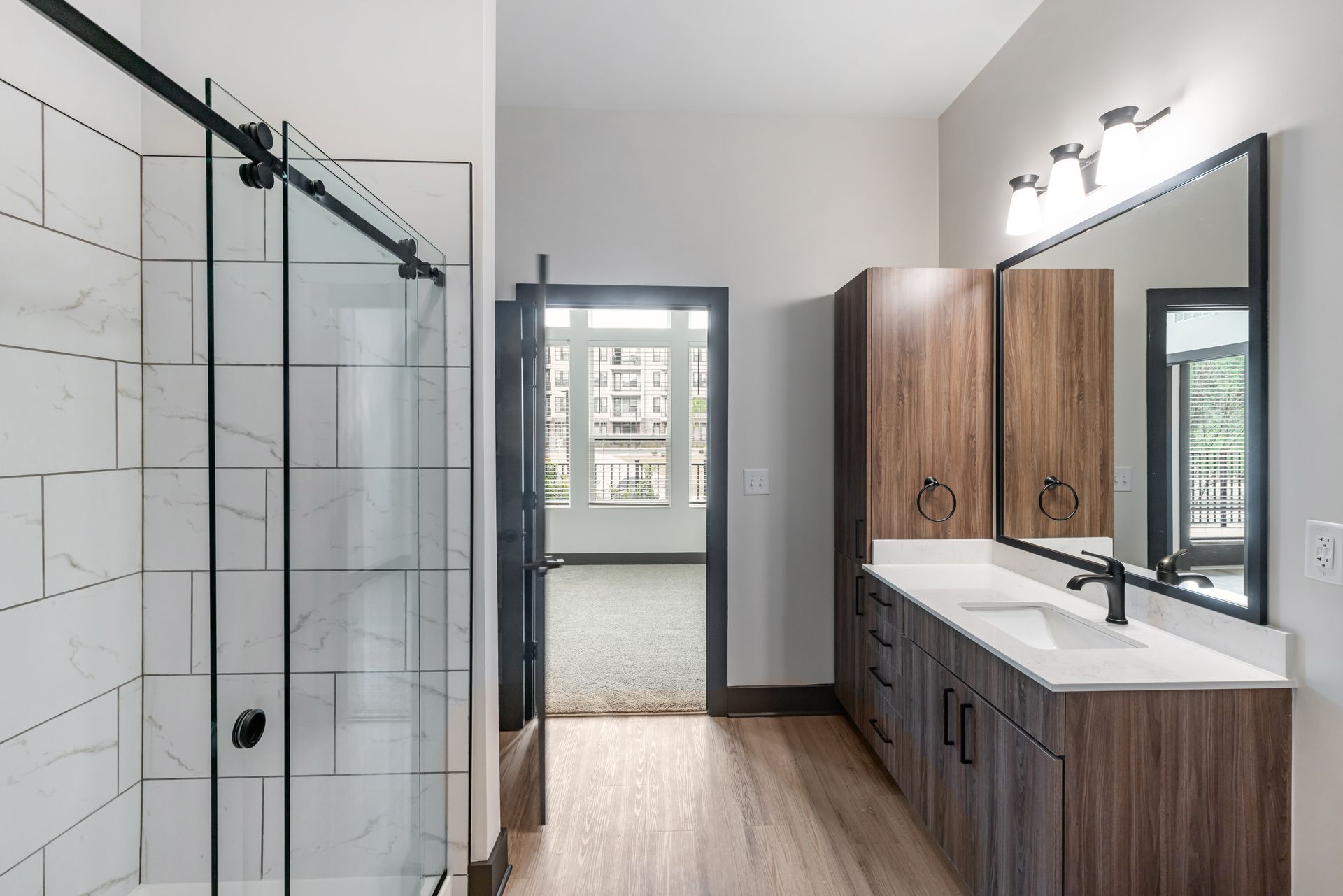 Modern bathroom with glass shower, wood vanity, large mirror, and white tile walls at Vela Park apartments in East Lake, Atlanta, GA.