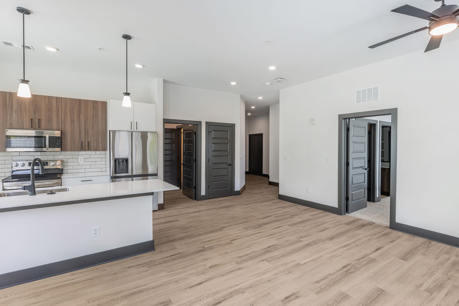 Empty modern kitchen and open living area with light wood floors, white walls, and black accents at Vela Park apartments in East Lake, Atlanta, GA.