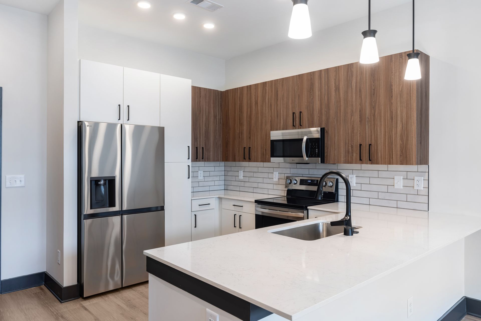 Modern kitchen with stainless steel appliances, wood cabinets, white countertops, and pendant lights at Vela Park apartments in East Lake, Atlanta, GA.