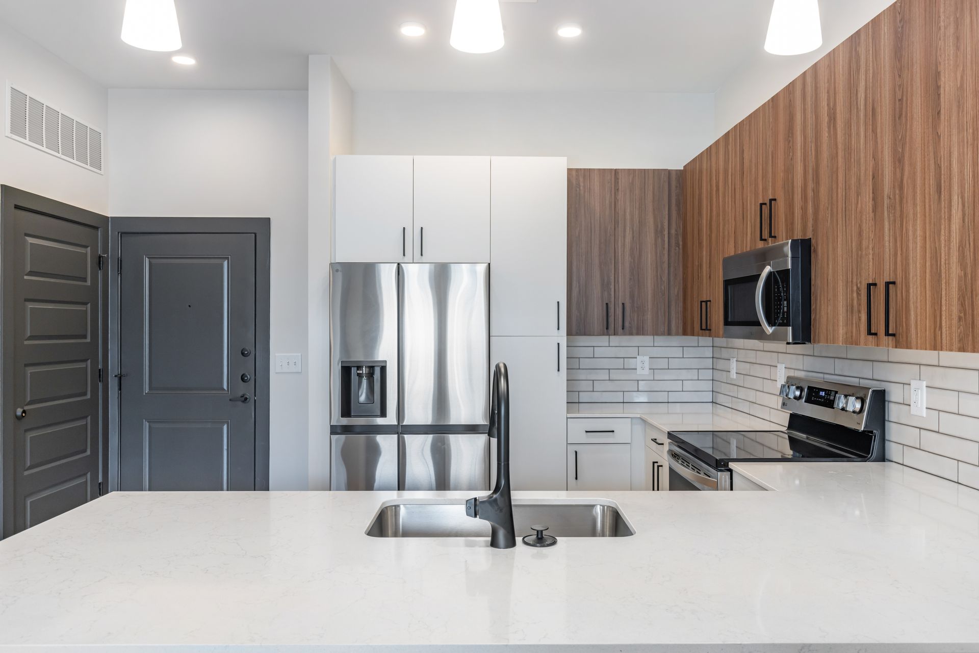 Modern kitchen with white island, stainless steel appliances, gray door, and wood cabinets at Vela Park apartments in East Lake, Atlanta, GA.