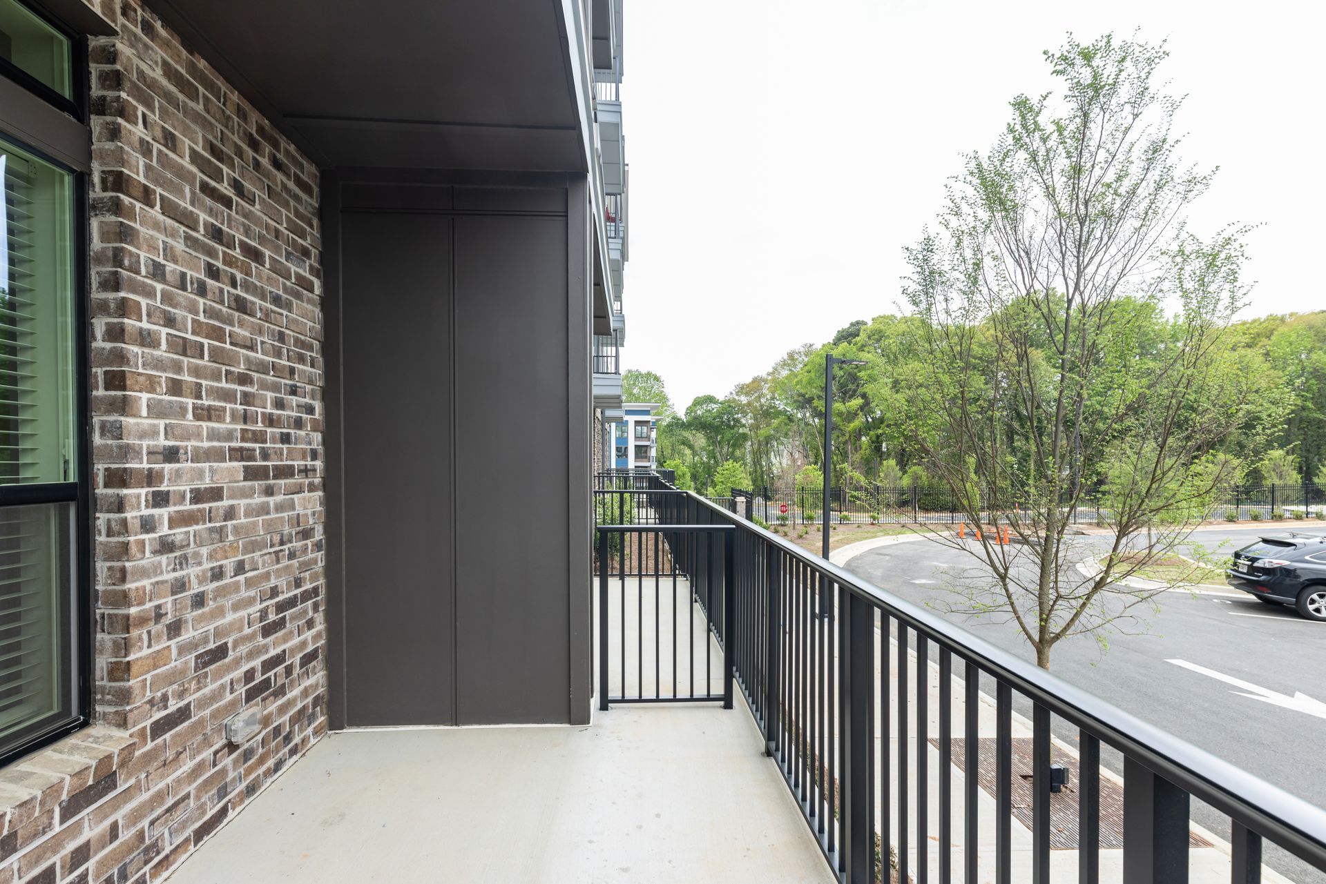 Apartment balcony overlooking a tree-lined street with black railing and brick wall at Vela Park apartments in East Lake, Atlanta, GA.