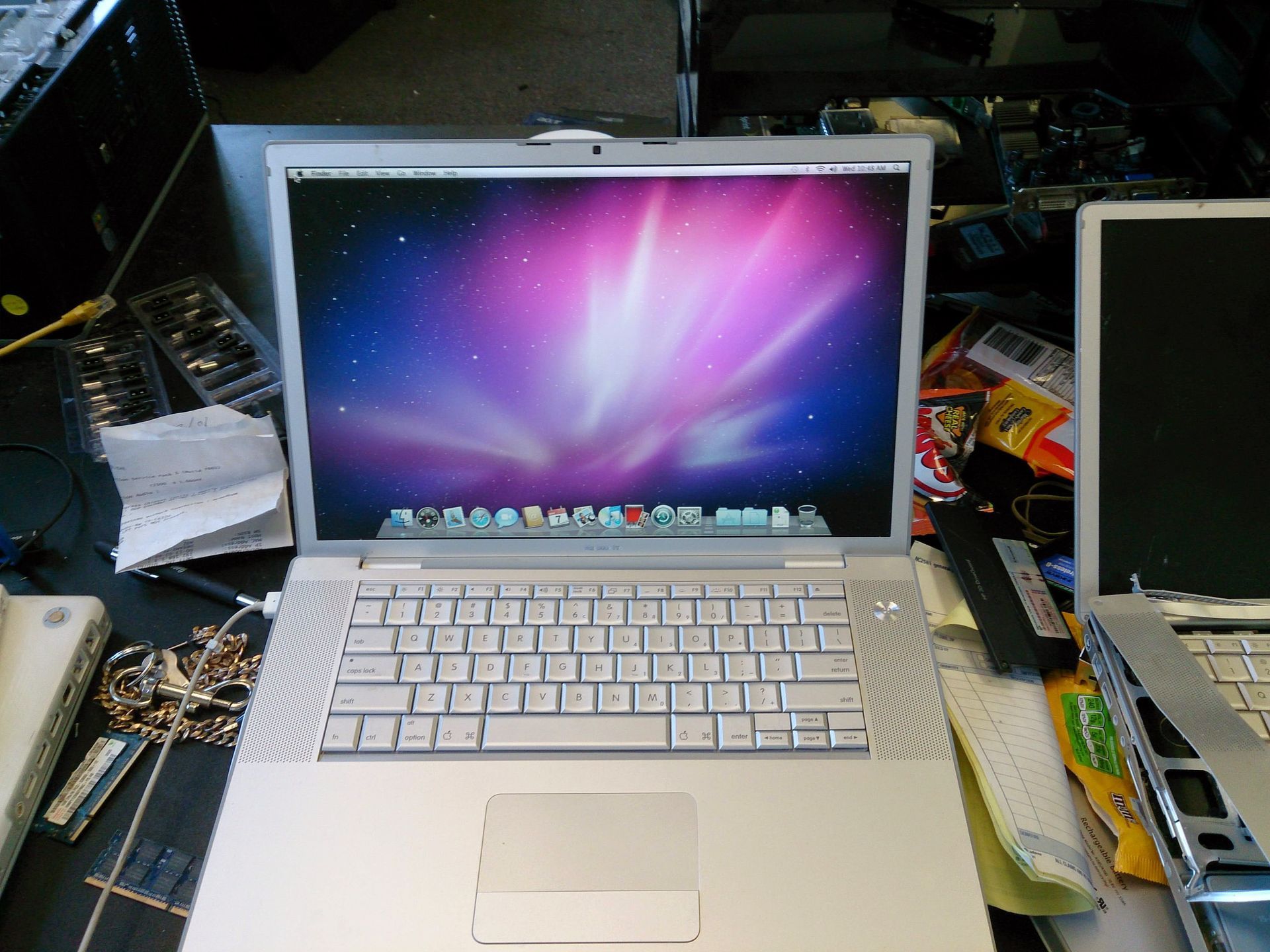 Silver Apple laptop, open, displaying colorful desktop; surrounded by computer parts on a cluttered table.
