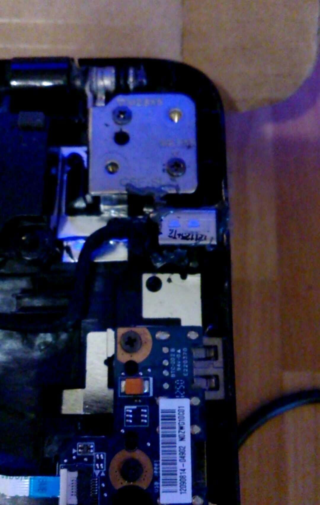 Laptop interior: hinge, USB port, and circuit board components. Black and blue colors dominate.