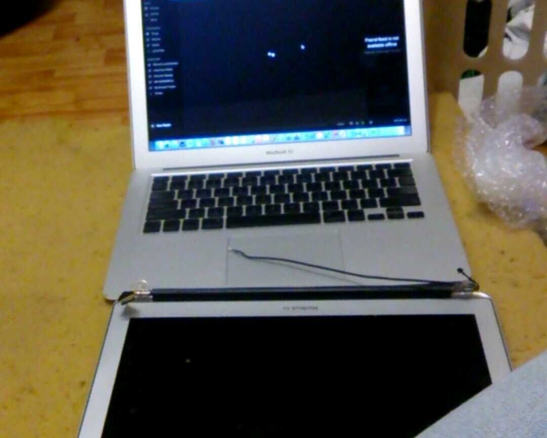 Laptop with detached screen, lying open on a surface. Cables exposed, showing repair in progress.