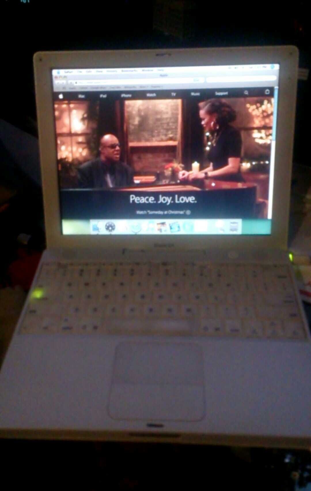 White laptop displaying a video of two people talking. The scene has dim lighting. The text on the video reads 