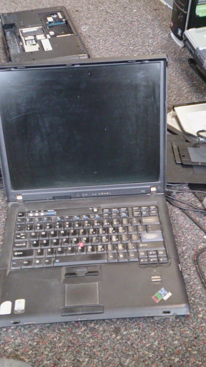 Black laptop, open, dirty keyboard, trackpad. Other disassembled computer parts are nearby.