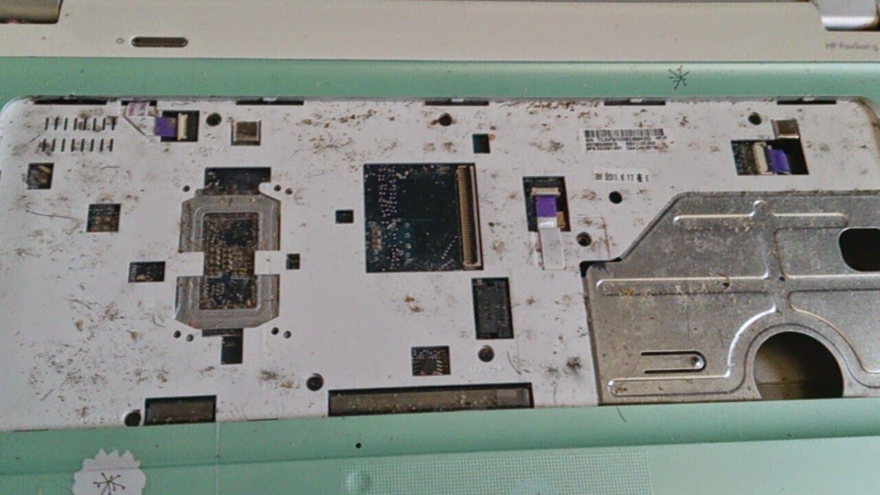 A disassembled laptop interior, revealing a metal plate with chips, circuits, and mounting points.