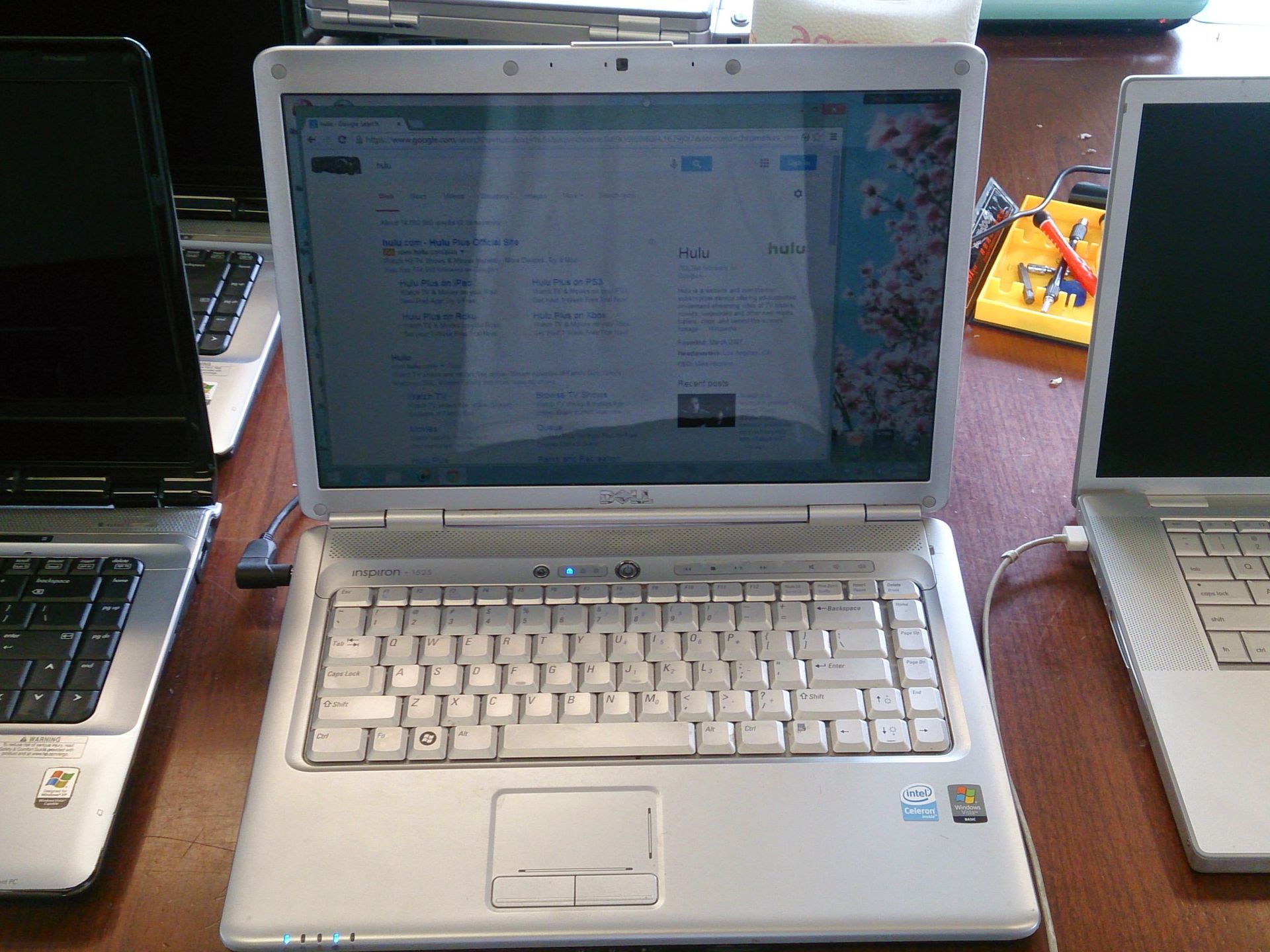 Silver Dell laptop open on a table, flanked by two closed laptops.