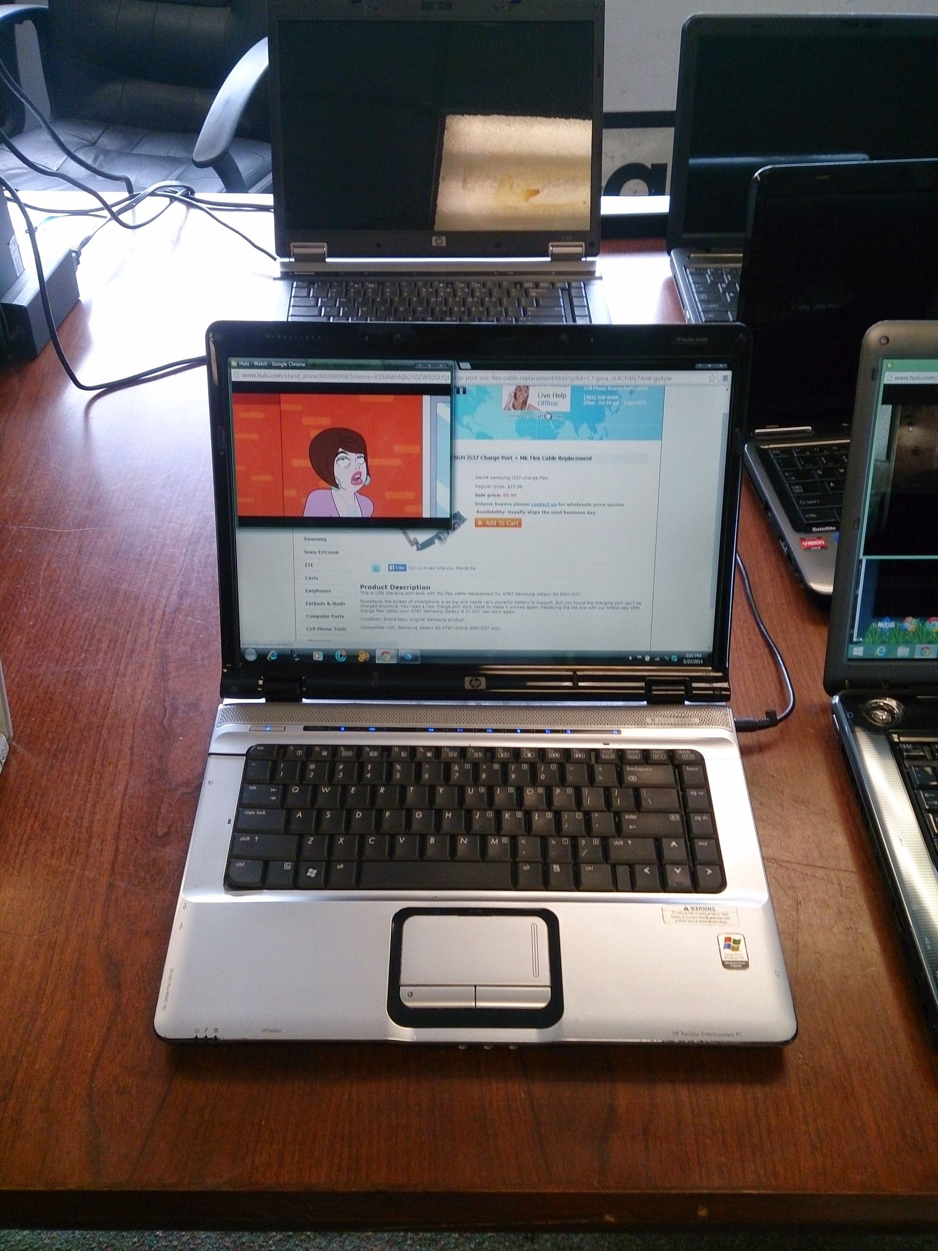 Laptop displaying a video with a person, surrounded by other laptops on a wooden table.