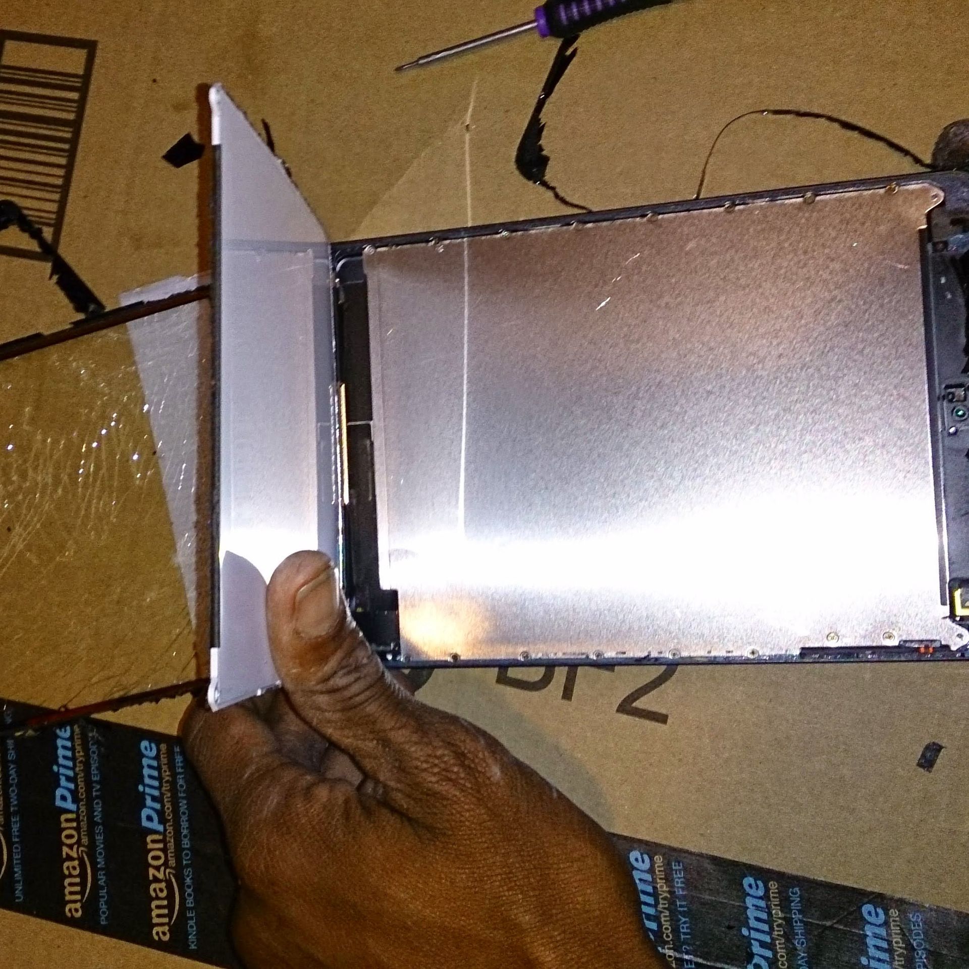 Hand holding a screen against a tablet, on a cardboard surface. Silver interior visible.
