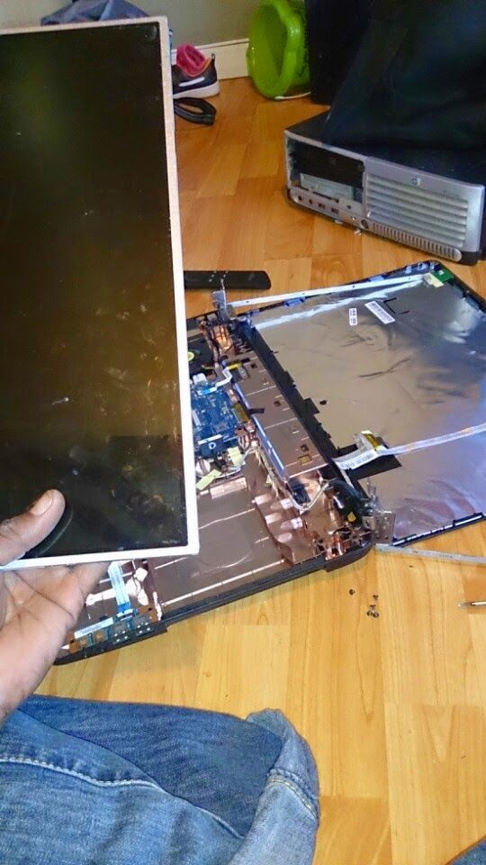 Person holding a laptop screen over the disassembled laptop on a wooden floor.