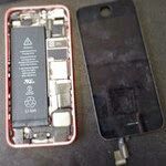 Disassembled smartphone showing battery, components, and screen lying next to the frame.