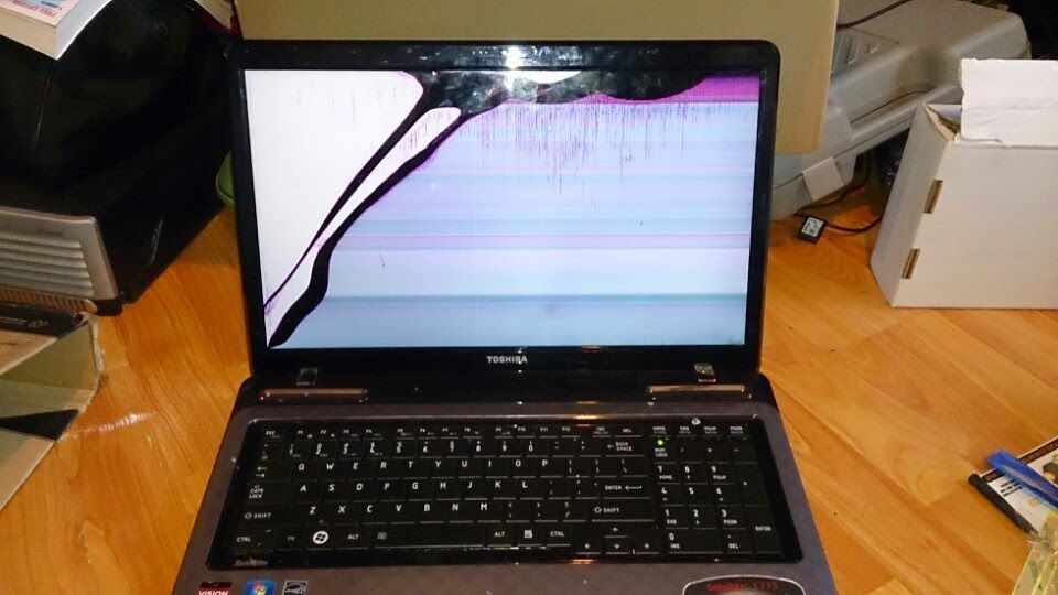 A damaged Toshiba laptop with a cracked screen, showing white and purple display damage.