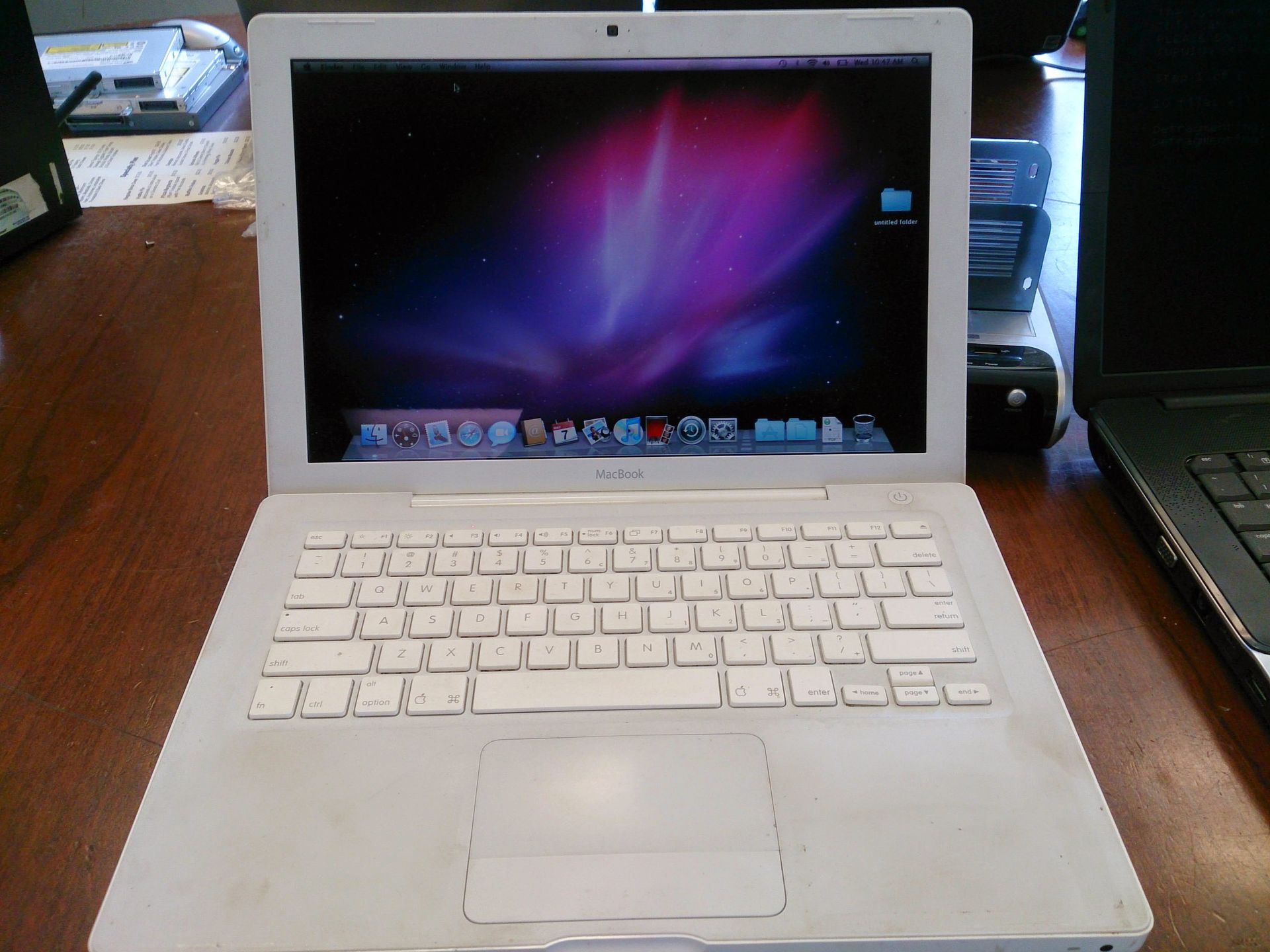 White MacBook laptop open on a wooden table, showing desktop with colorful background.