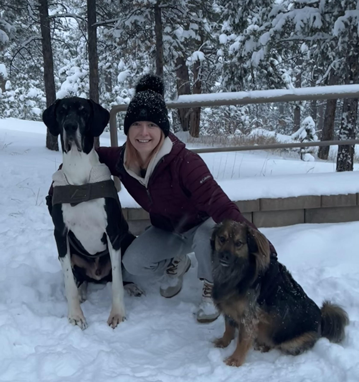 A woman kneeling down with two dogs in the snow