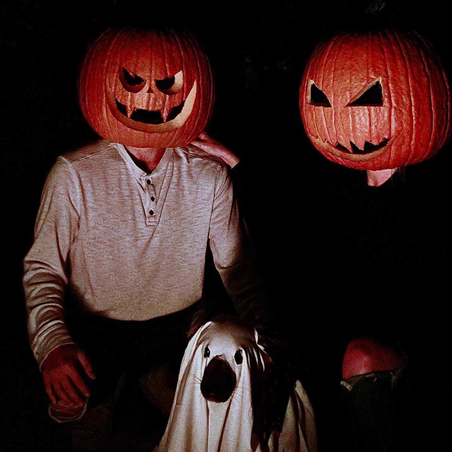Two people with pumpkins on their heads are standing next to a ghost.