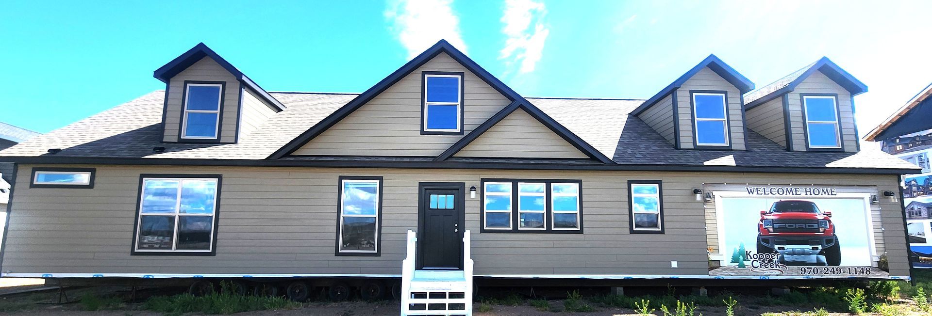 Front view of a gray house with blue trim, dormer windows, and a basketball hoop in the driveway
