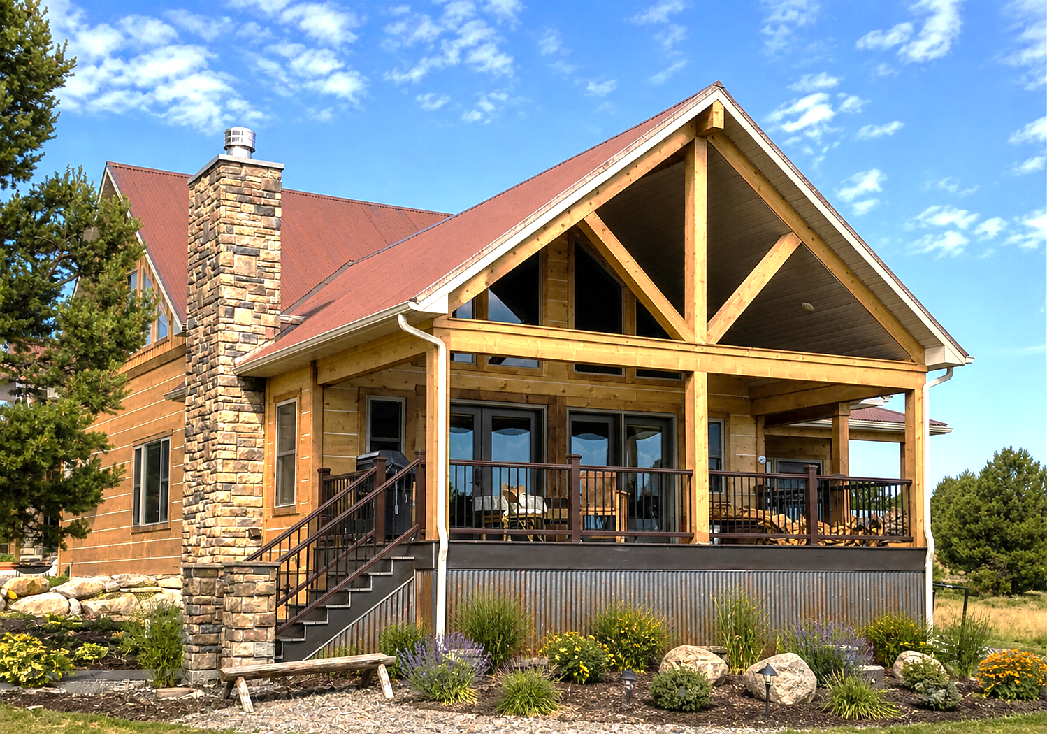 Rustic log cabin with red roof, stone chimney, and covered porch in a sunny landscape