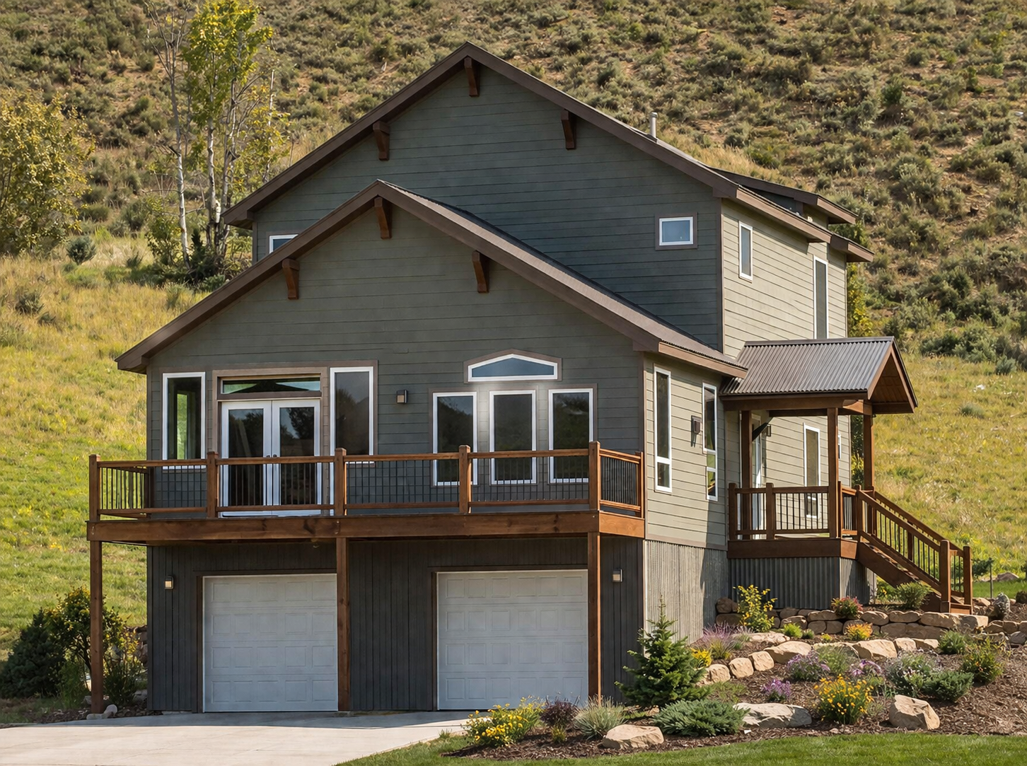 Modern two-story house with a wooden deck, two garage doors, and a hillside backdrop