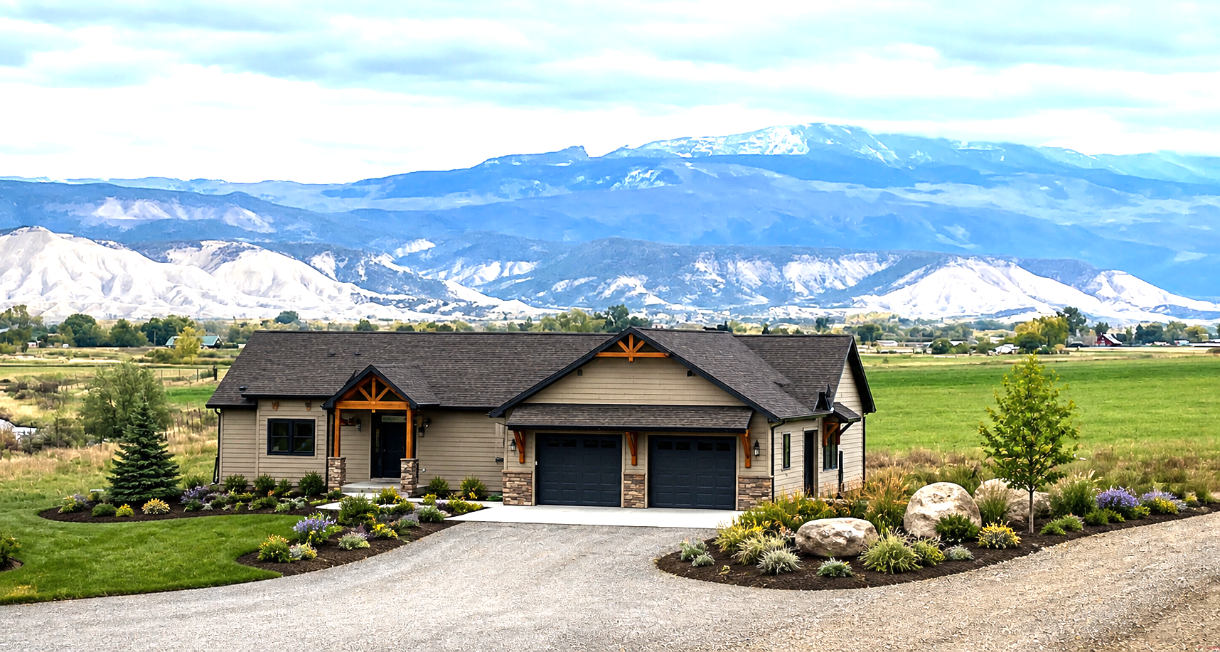 Modern house with three-car garage on a gravel drive, set before green fields and snowy mountains under a blue sky