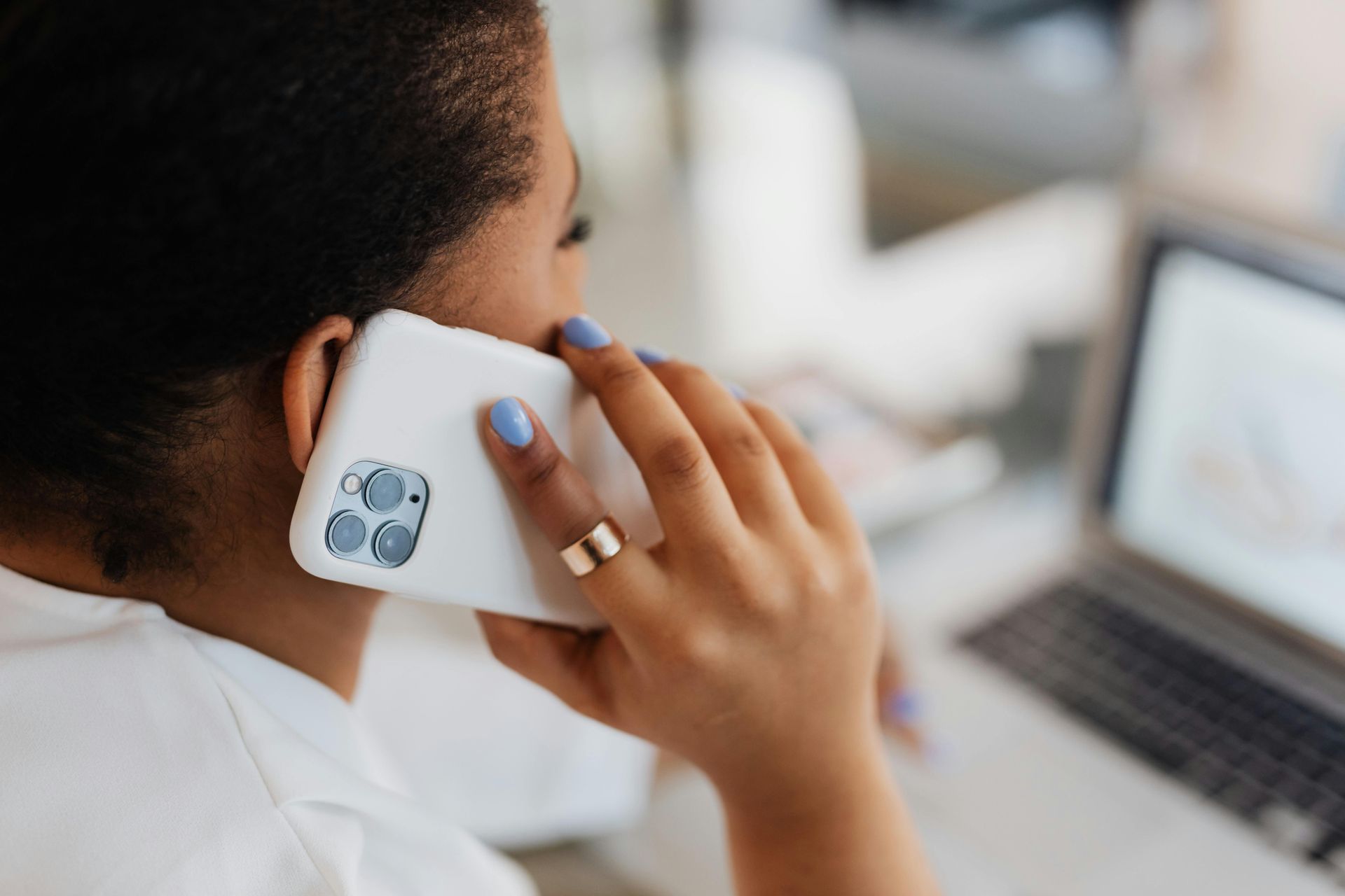 Woman with short dark hair on a phone call, working on a laptop in an office.