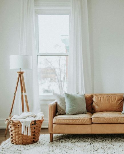 Cozy living room with tan sofa, wicker basket, floor lamp, white curtains, and window.
