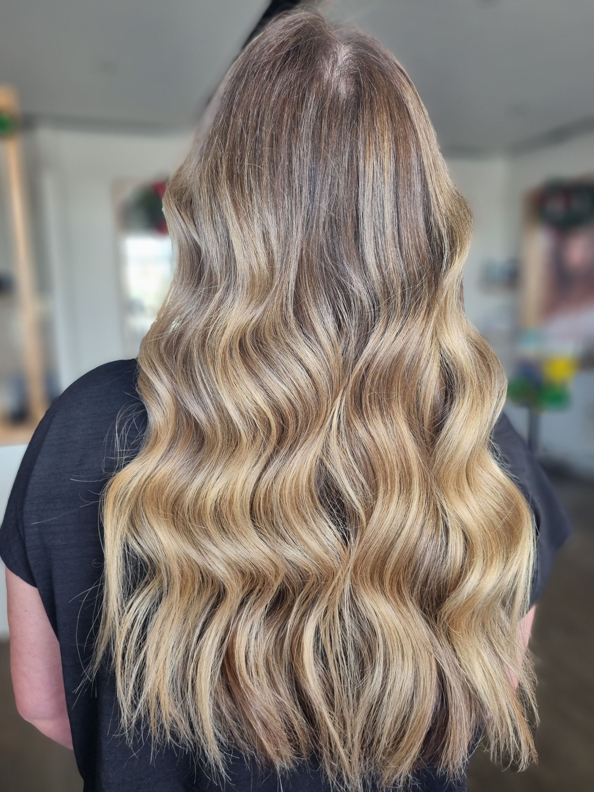 A Woman With Long Wavy Blonde Hair Is Wearing A Black Shirt — Arabella Hair Design in Sebastopol, VIC