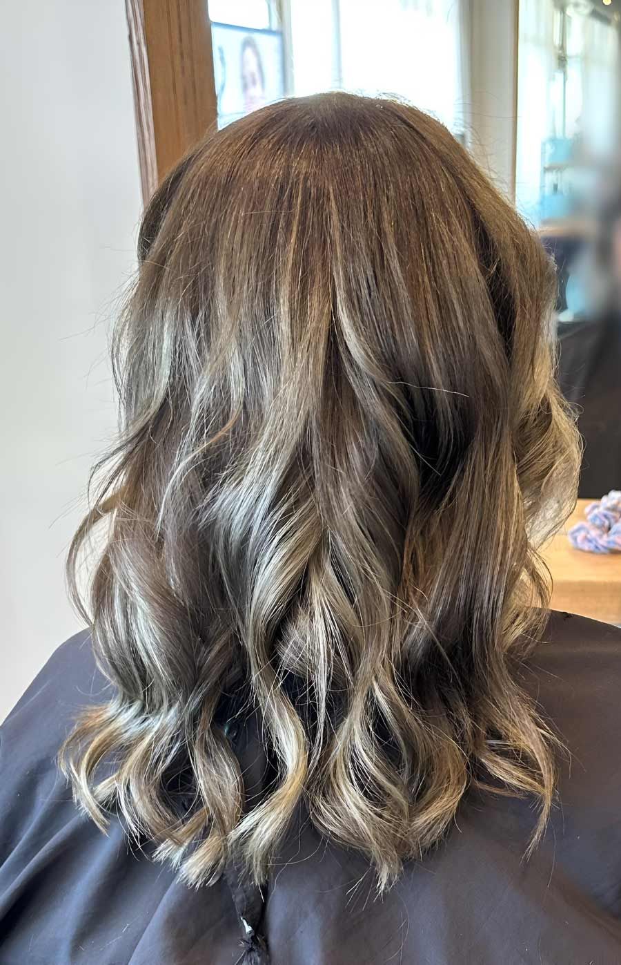 A Woman With Long Wavy Hair Is Sitting In A Chair In Front Of A Mirror — Arabella Hair Design in Sebastopol, VIC