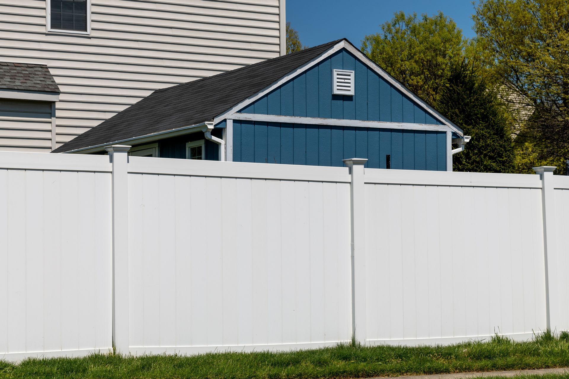 A white fence surrounds a blue garage in front of a house.