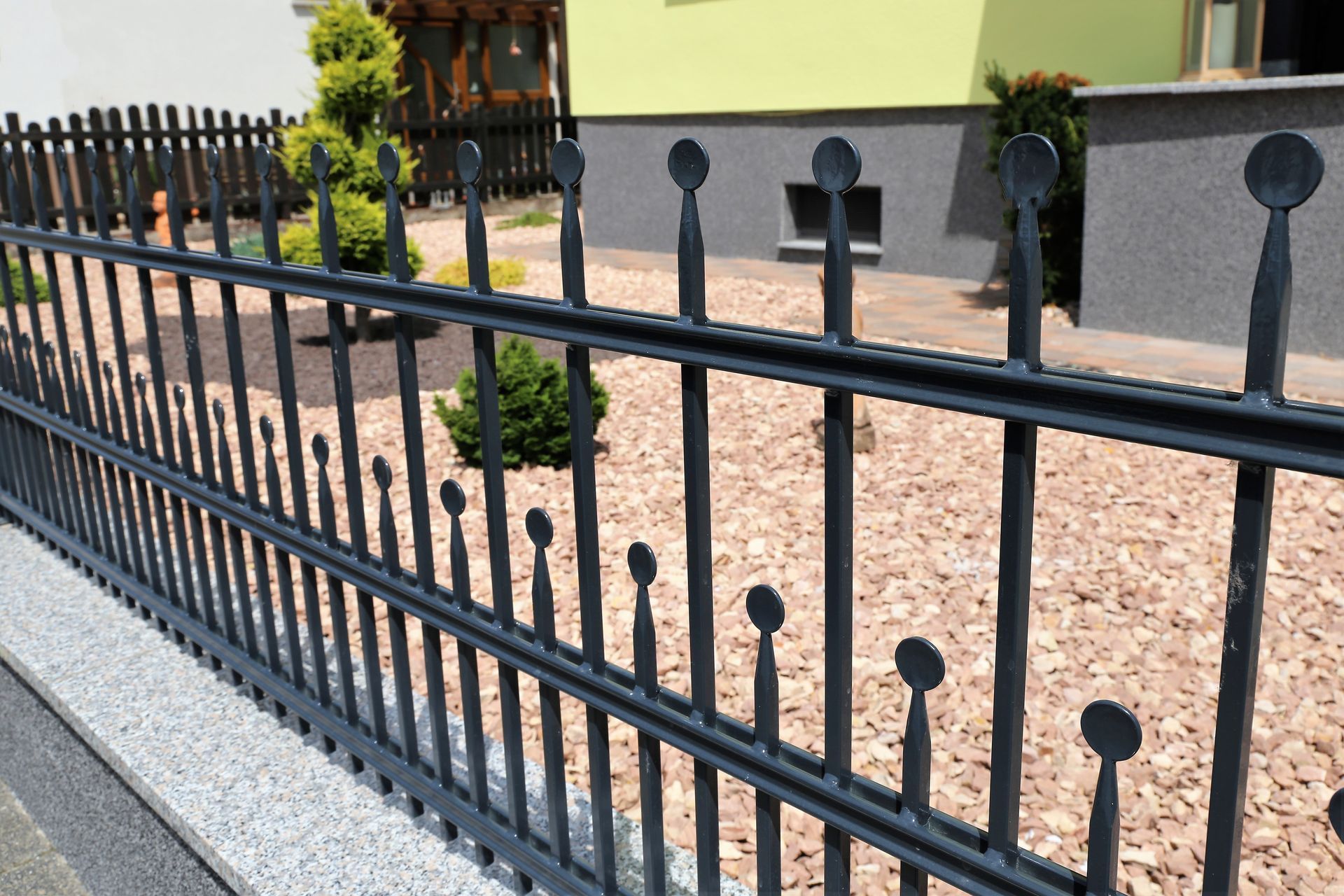 A black wrought iron fence is surrounded by gravel in front of a house.
