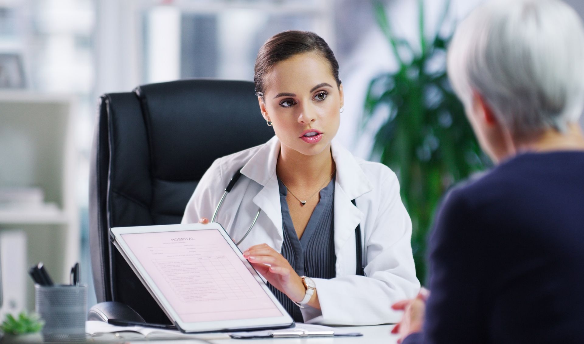 A doctor is sitting at a desk talking to an older woman.