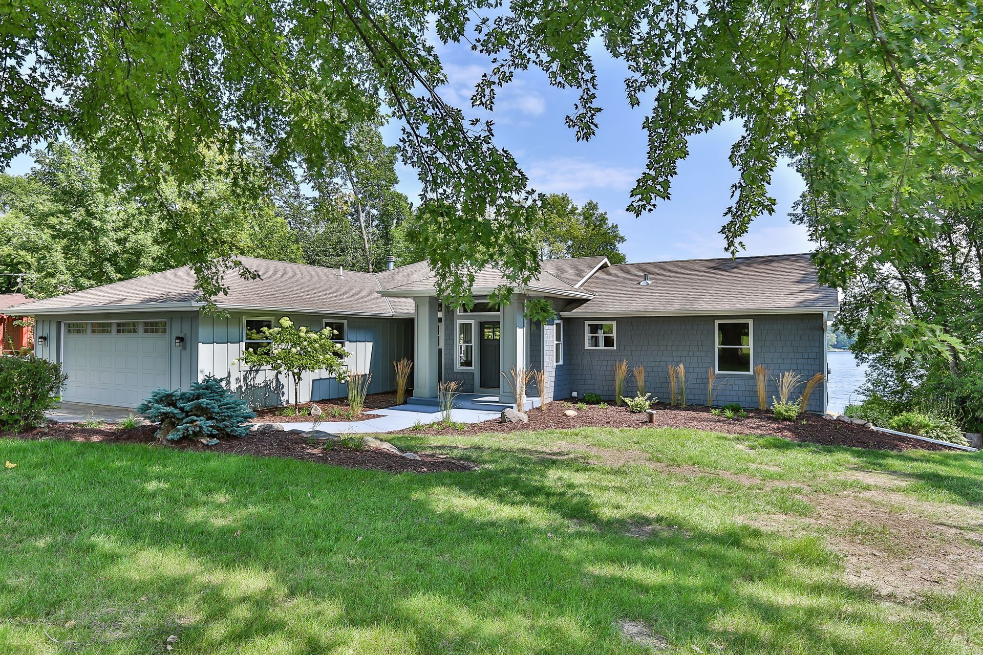 Blue ranch-style house with garage, set amidst green grass and trees.