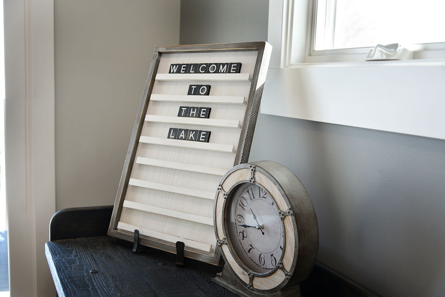 Letter board saying "Welcome to the lake" next to a nautical clock on a shelf.