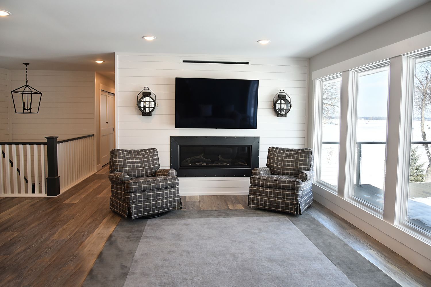 Living room with a fireplace, TV, and two patterned armchairs. Large windows on the right.