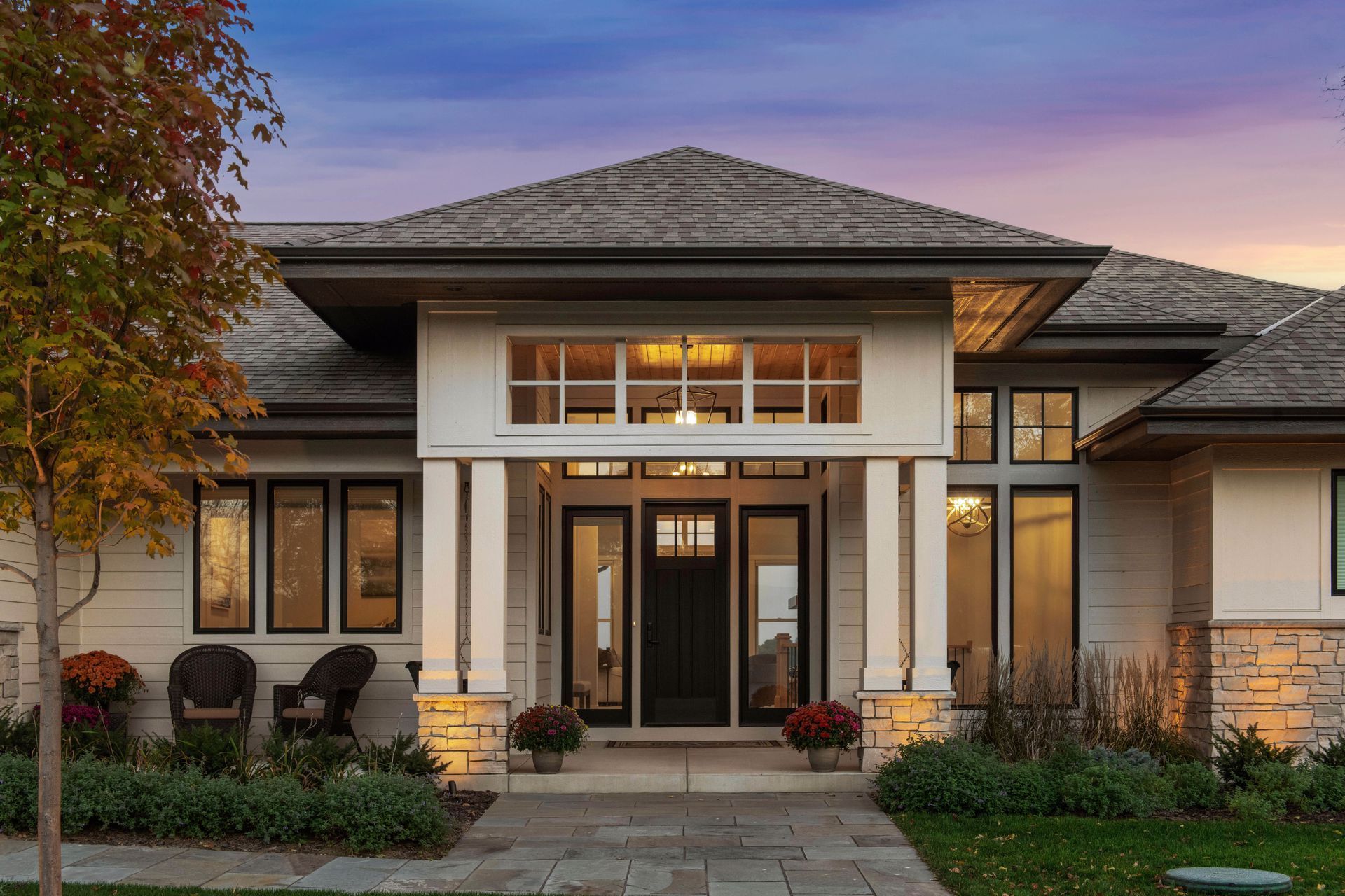 Exterior of a white house with a dark door, stone facade, columns, and a landscaped walkway.
