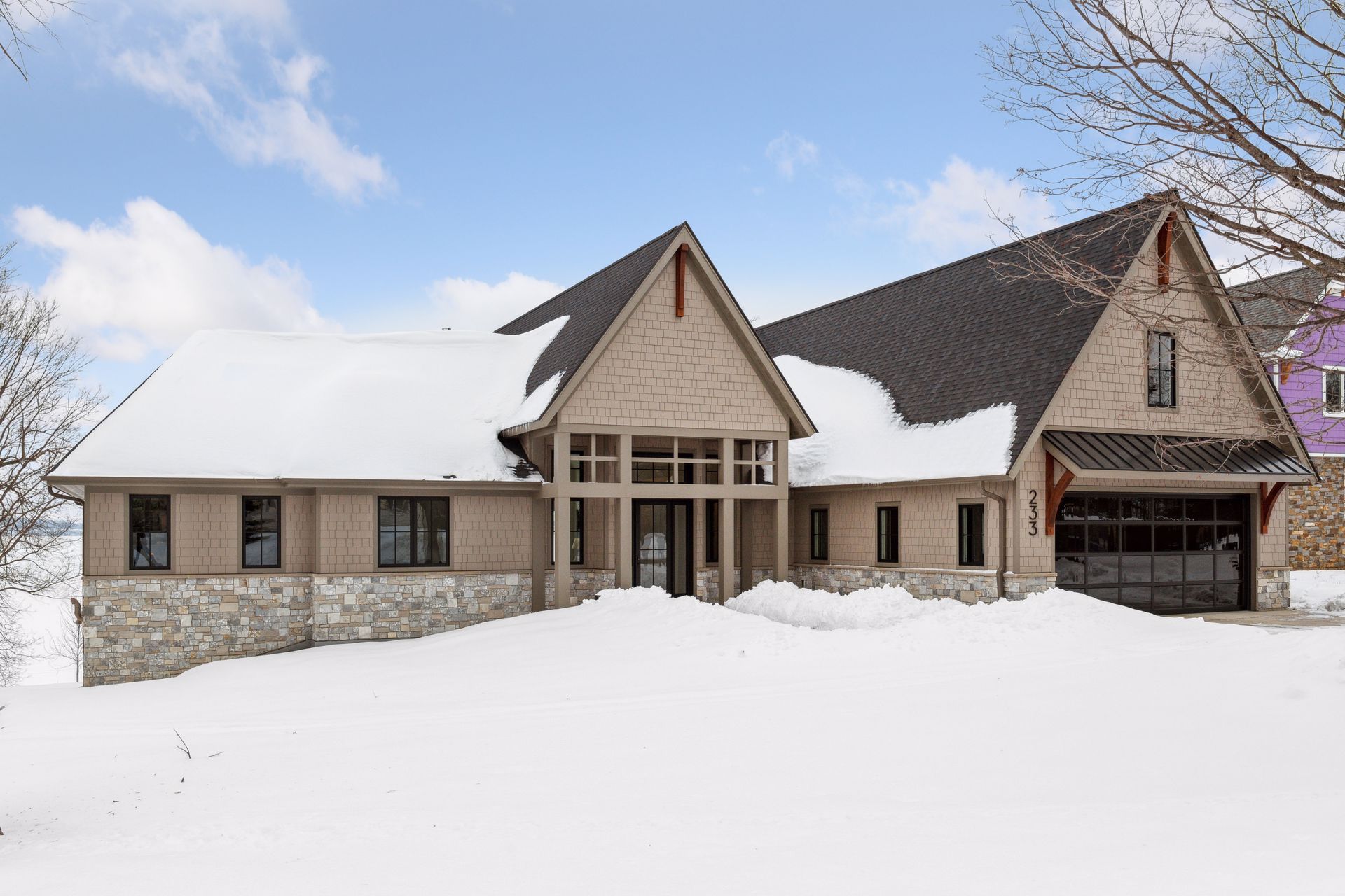 Snow-covered beige house with a dark garage door, against a cloudy sky.