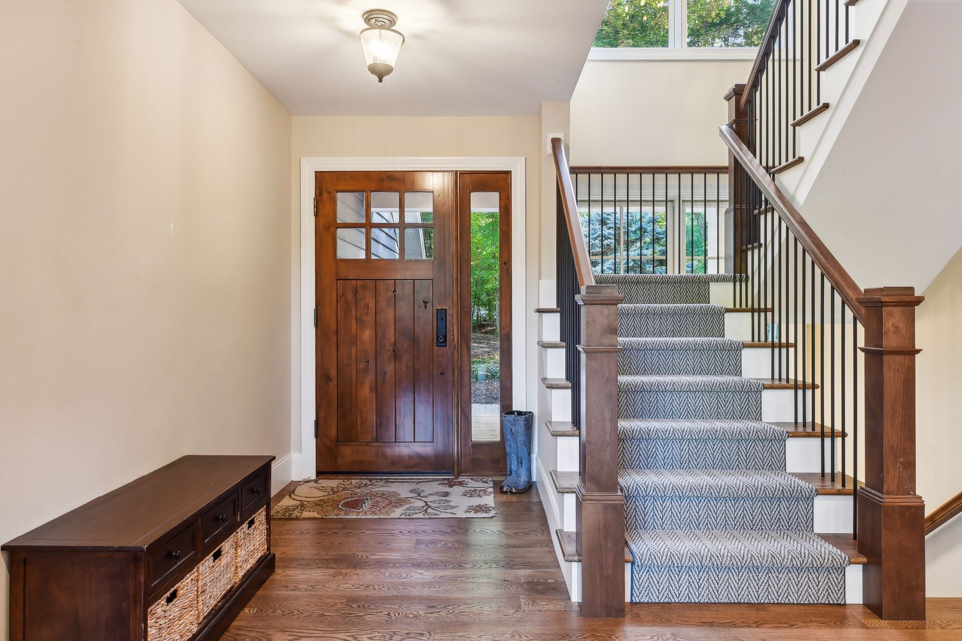 Entryway with wooden door, stairs, and bench with baskets.  Wood floors and neutral-colored walls.